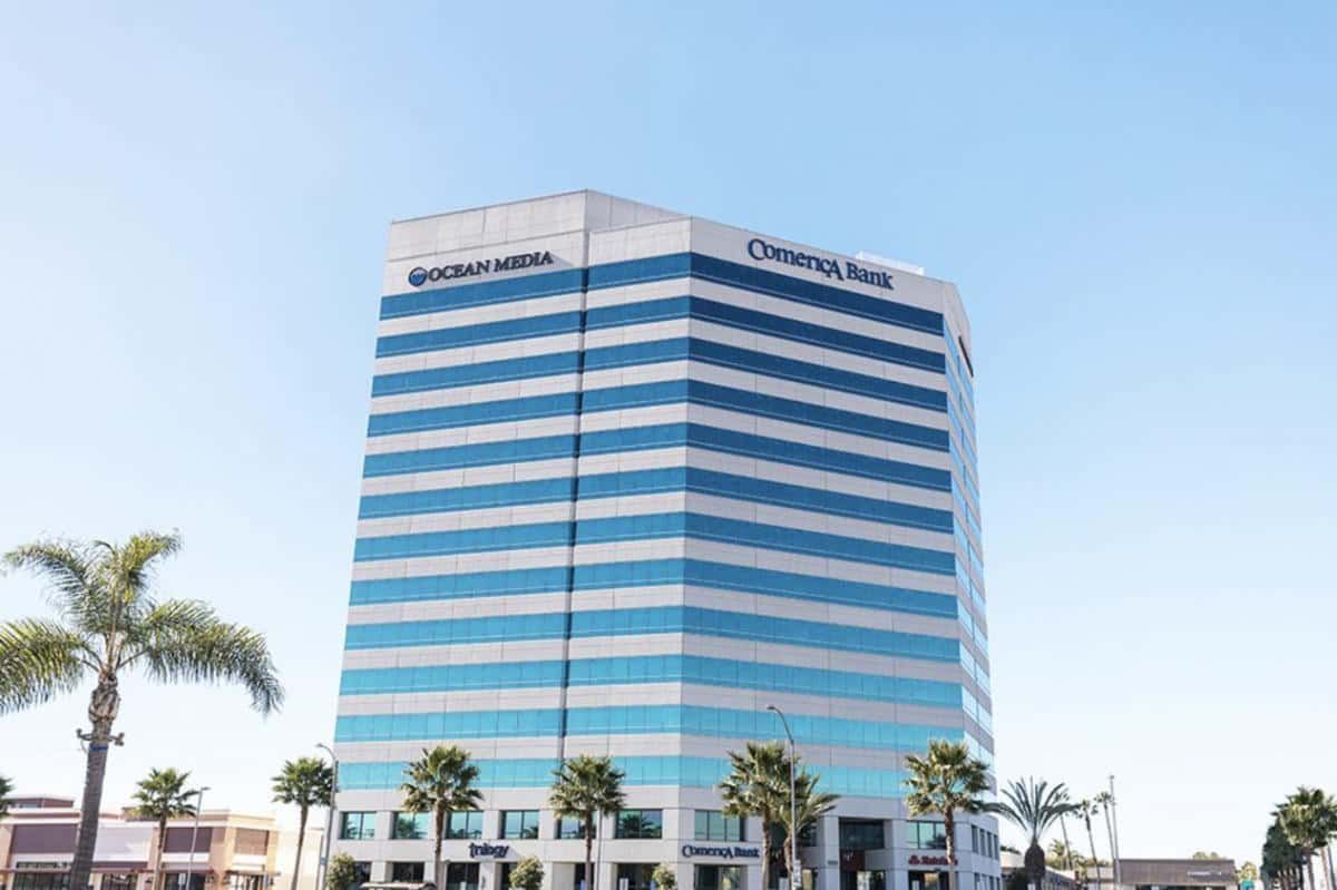 A tall building with a lot of windows and palm trees in front of it.
