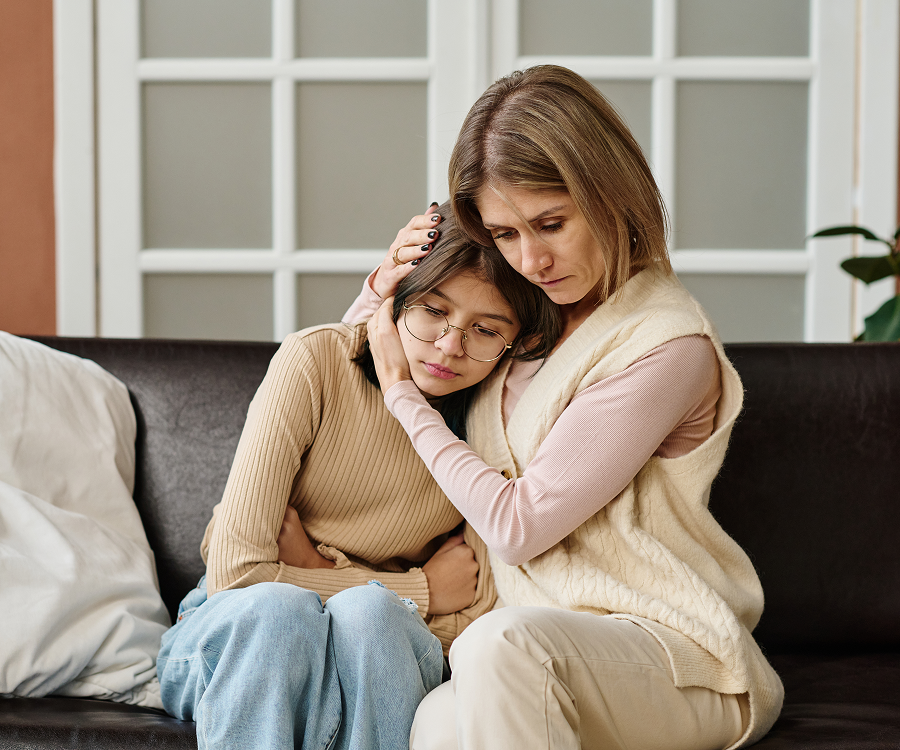 A mother and daughter are sitting on a couch hugging each other.