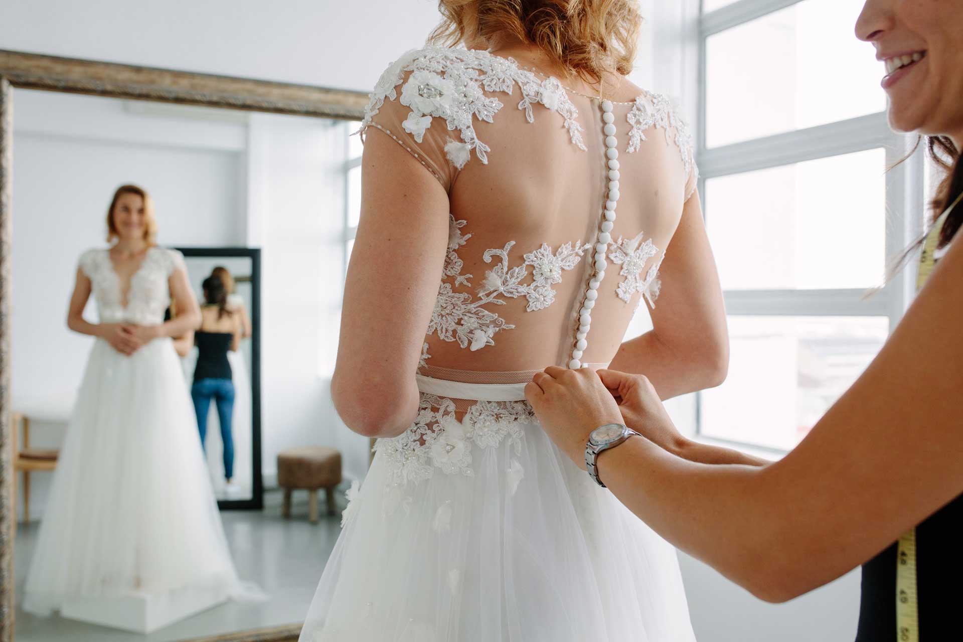 A woman is trying on a wedding dress in front of a mirror.