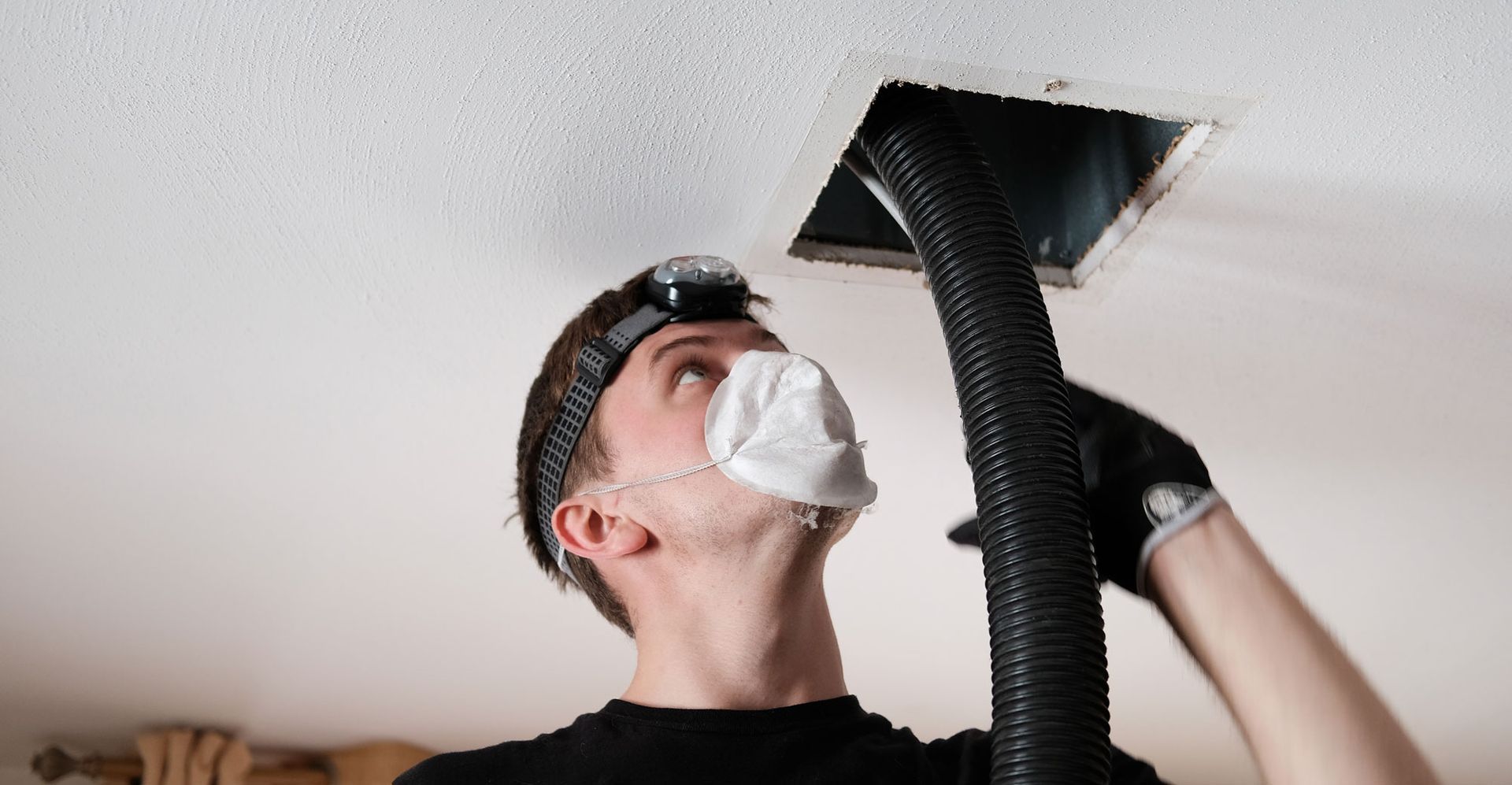 A man is standing on a ladder cleaning an air vent.