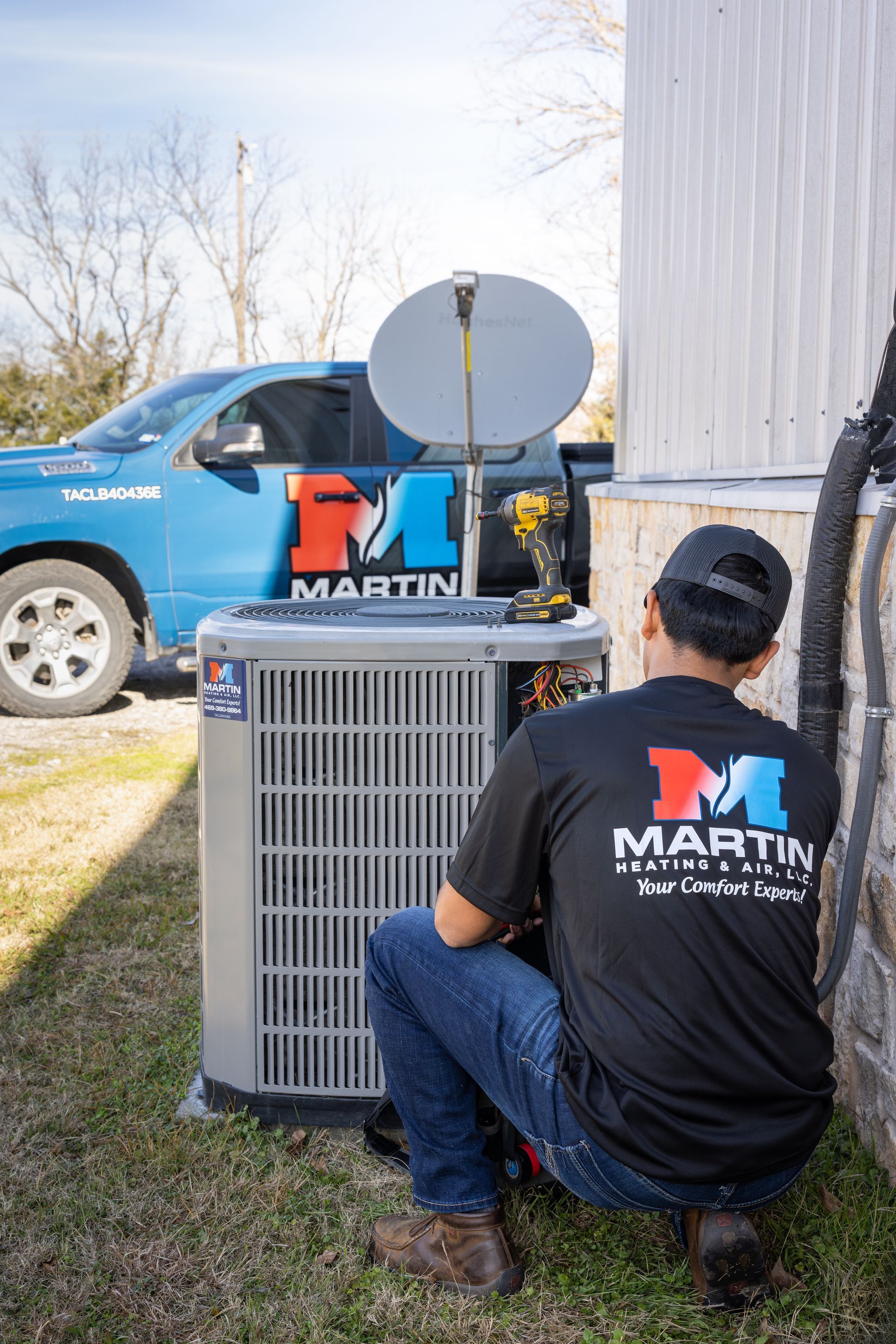 Two men are working on an air conditioner outside of a brick building.