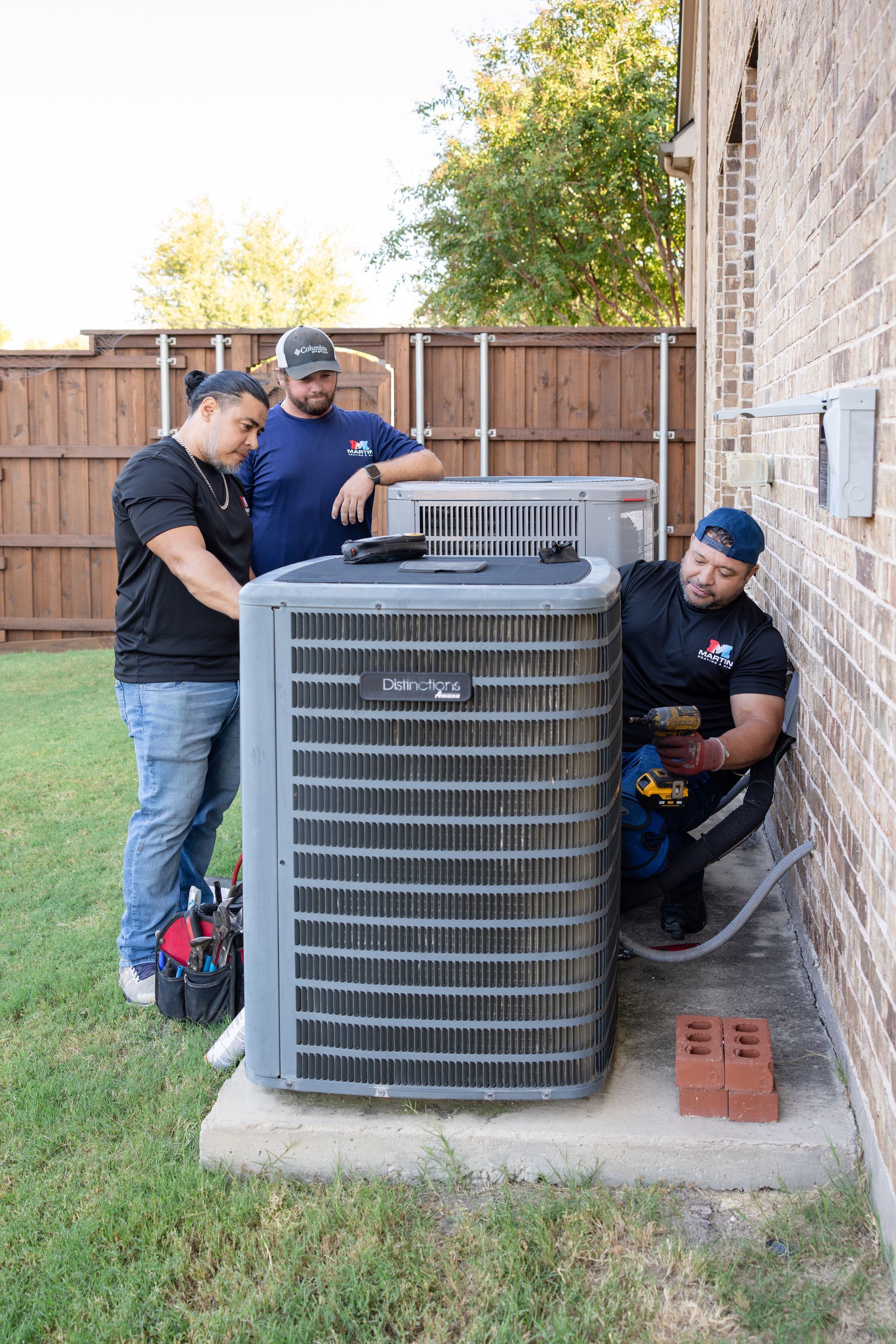 Two men are working on an air conditioner outside of a building.