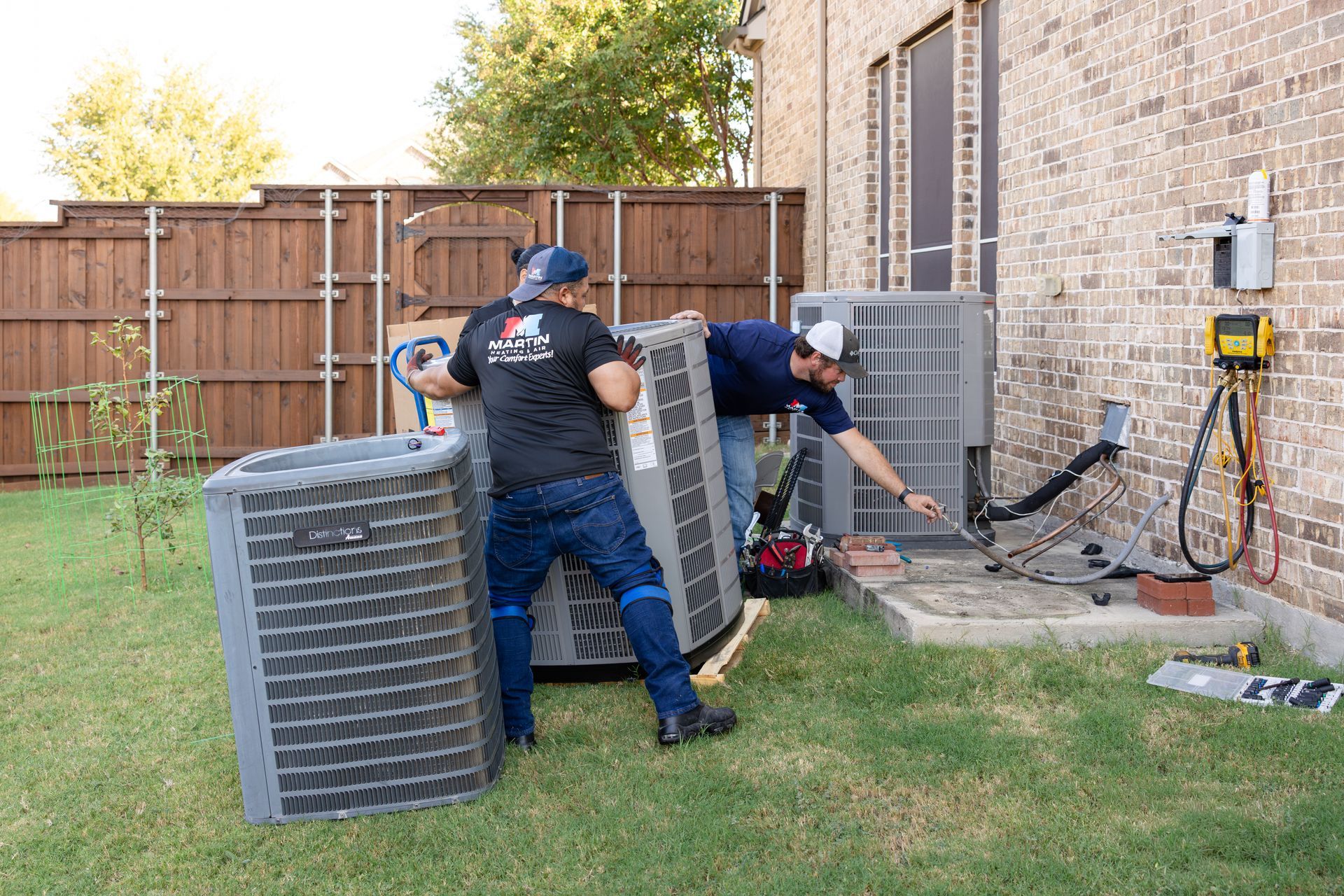 Two air conditioners are sitting on gravel outside of a house.