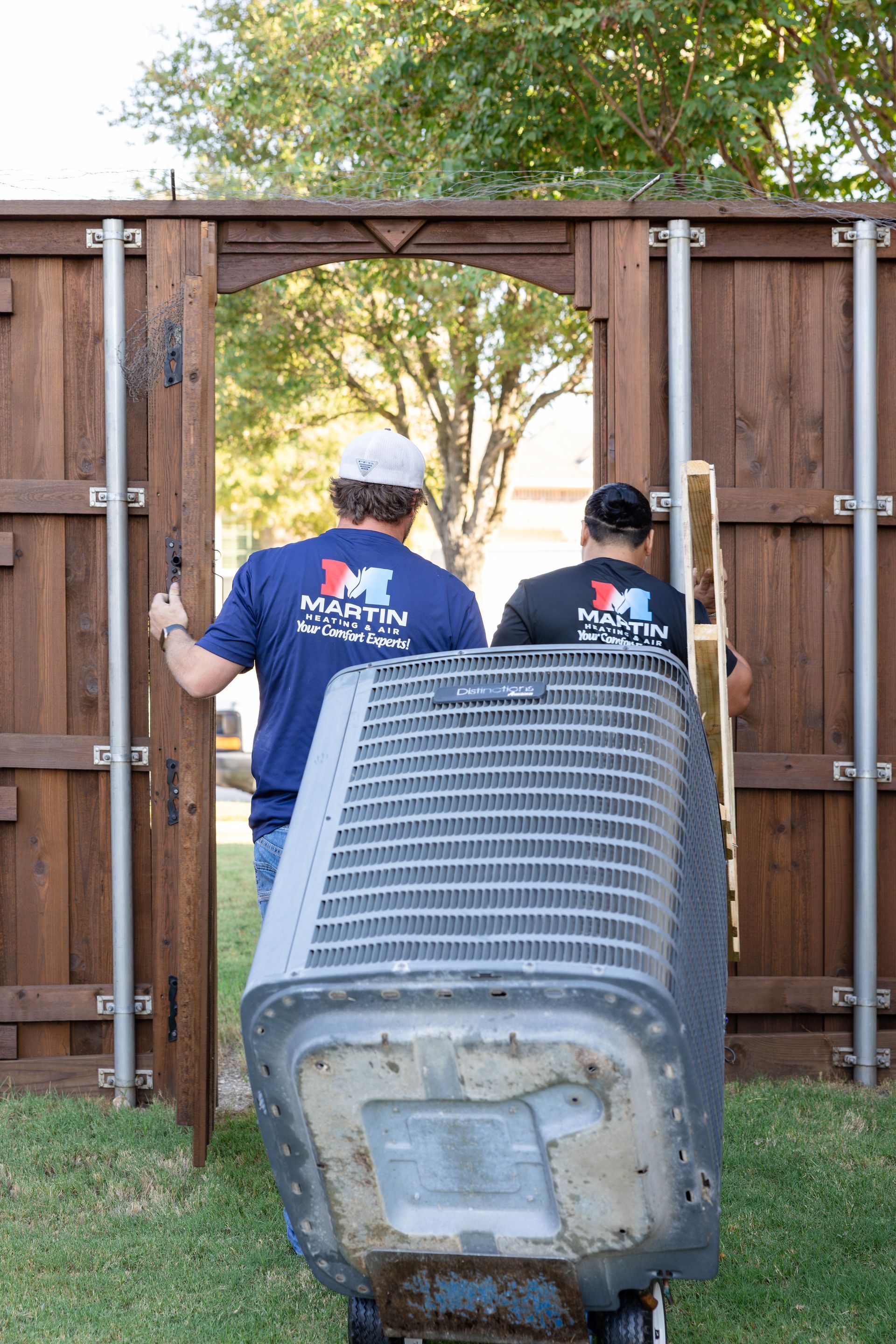 A man is standing on a ladder installing an air conditioner on the side of a building.