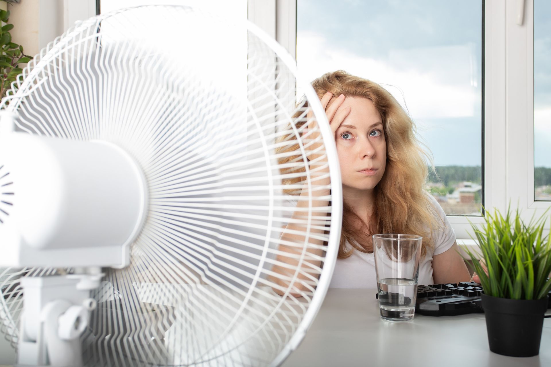 Woman blowing a fan to prevent sweating and stay comfortable in the heat in the office in Wylie, TX.