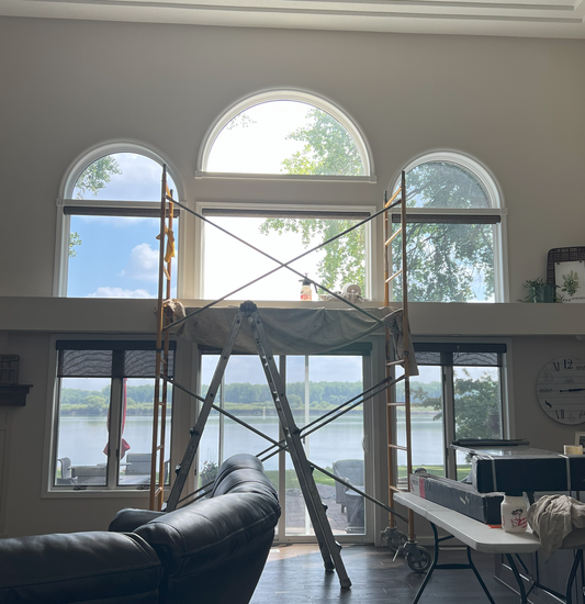 A living room with a scaffolding in front of a large window with a view of a lake.