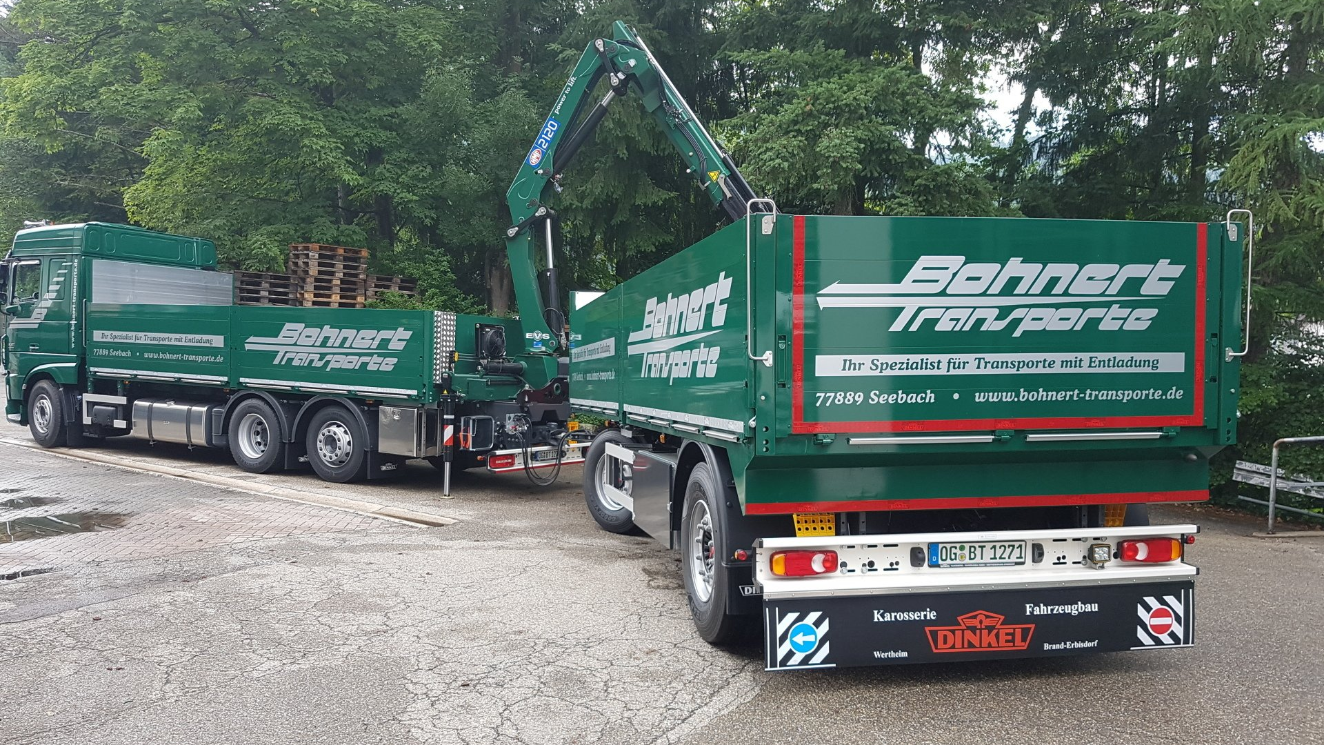 Ein grüner Lastwagen mit einem Kran auf der Ladefläche steht auf einem Schotterplatz.