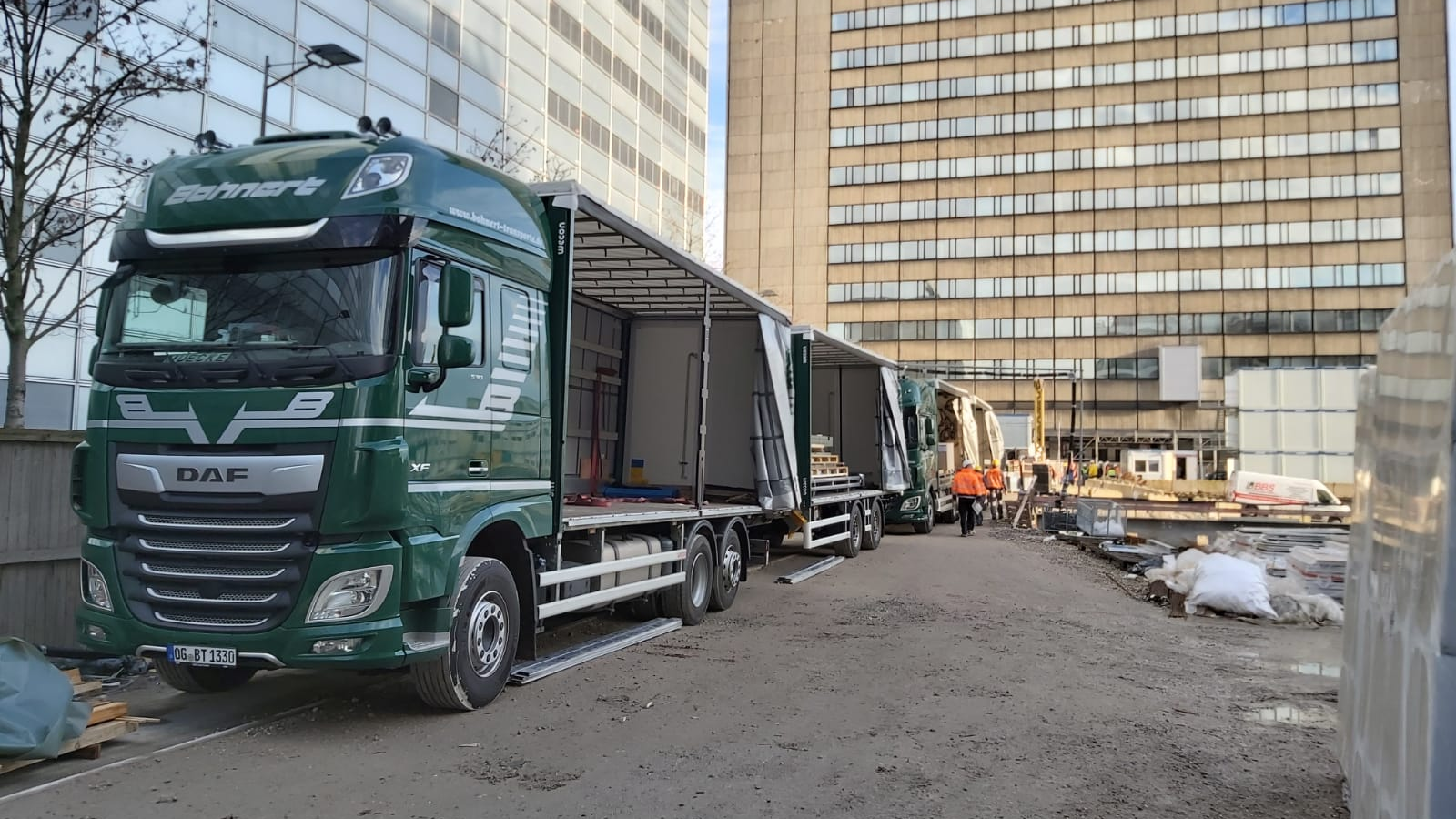 Ein grüner Lastwagen steht am Straßenrand vor einem Gebäude.