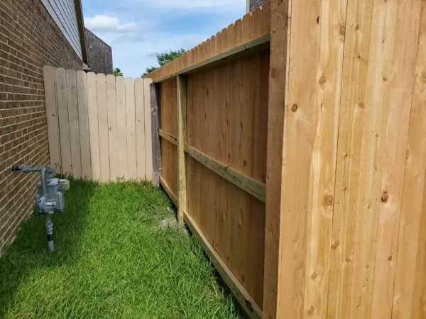 Wooden fences of different colors flank a grassy area beside a brick building.