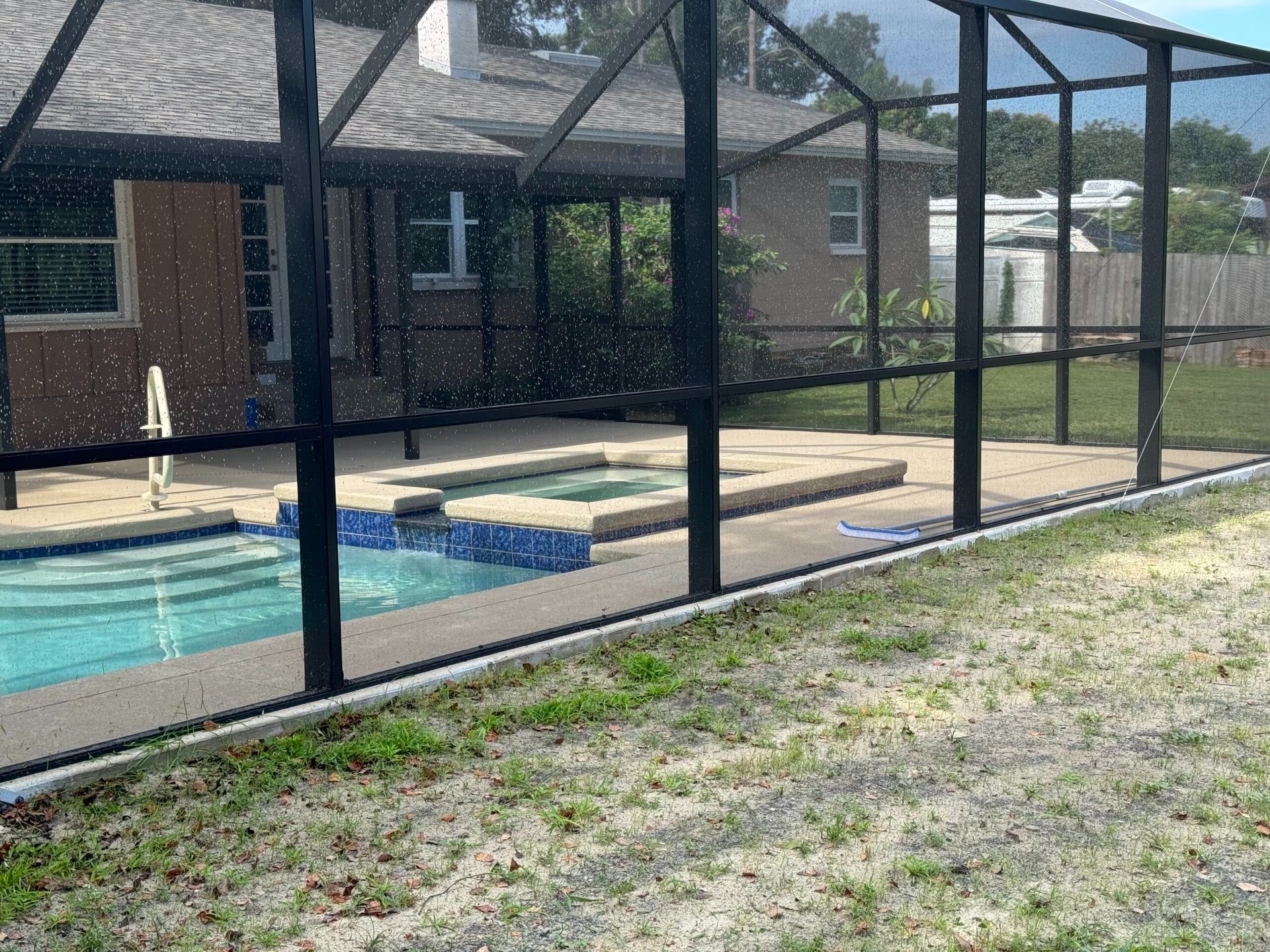 Screened-in swimming pool with a spa. Black framing, blue water, concrete deck, and green grass.