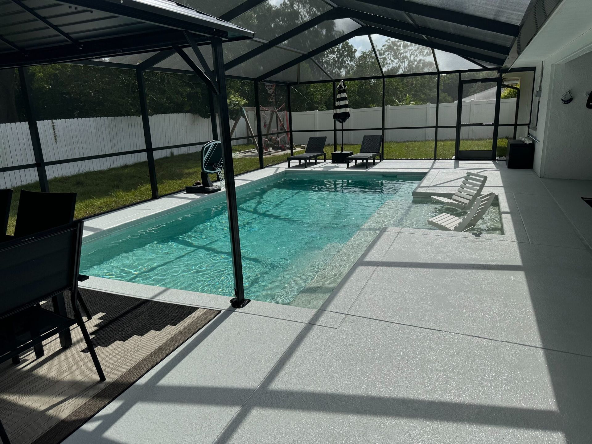 A screened-in pool area with a rectangular pool of turquoise water, surrounded by a patio and lounge chairs.