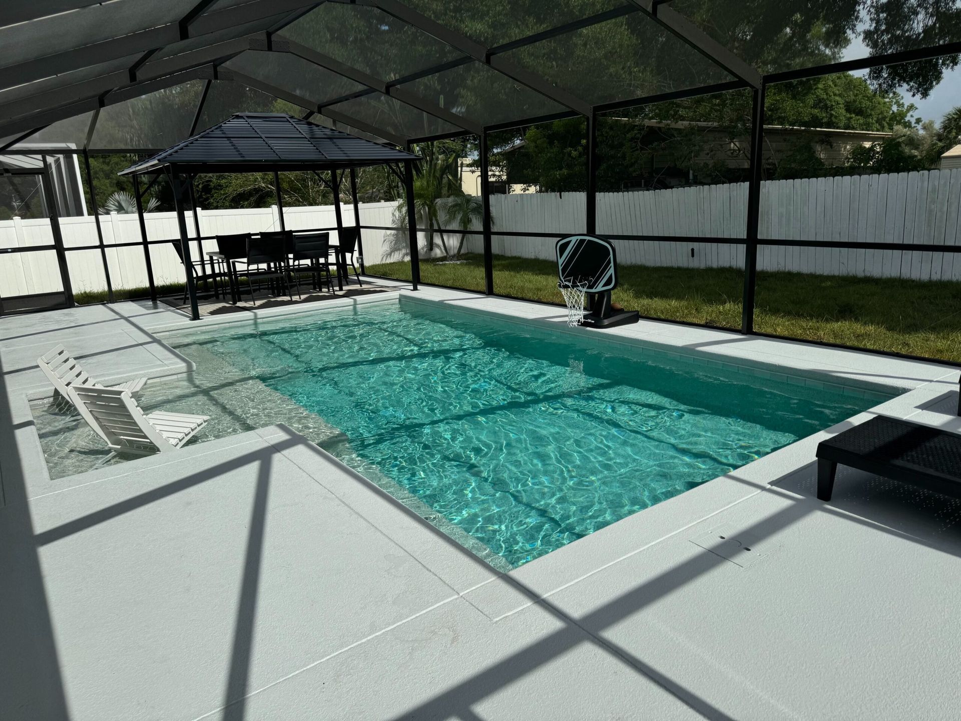 A screened-in backyard pool with a gazebo-covered dining area and a lounge chair. The water is teal.