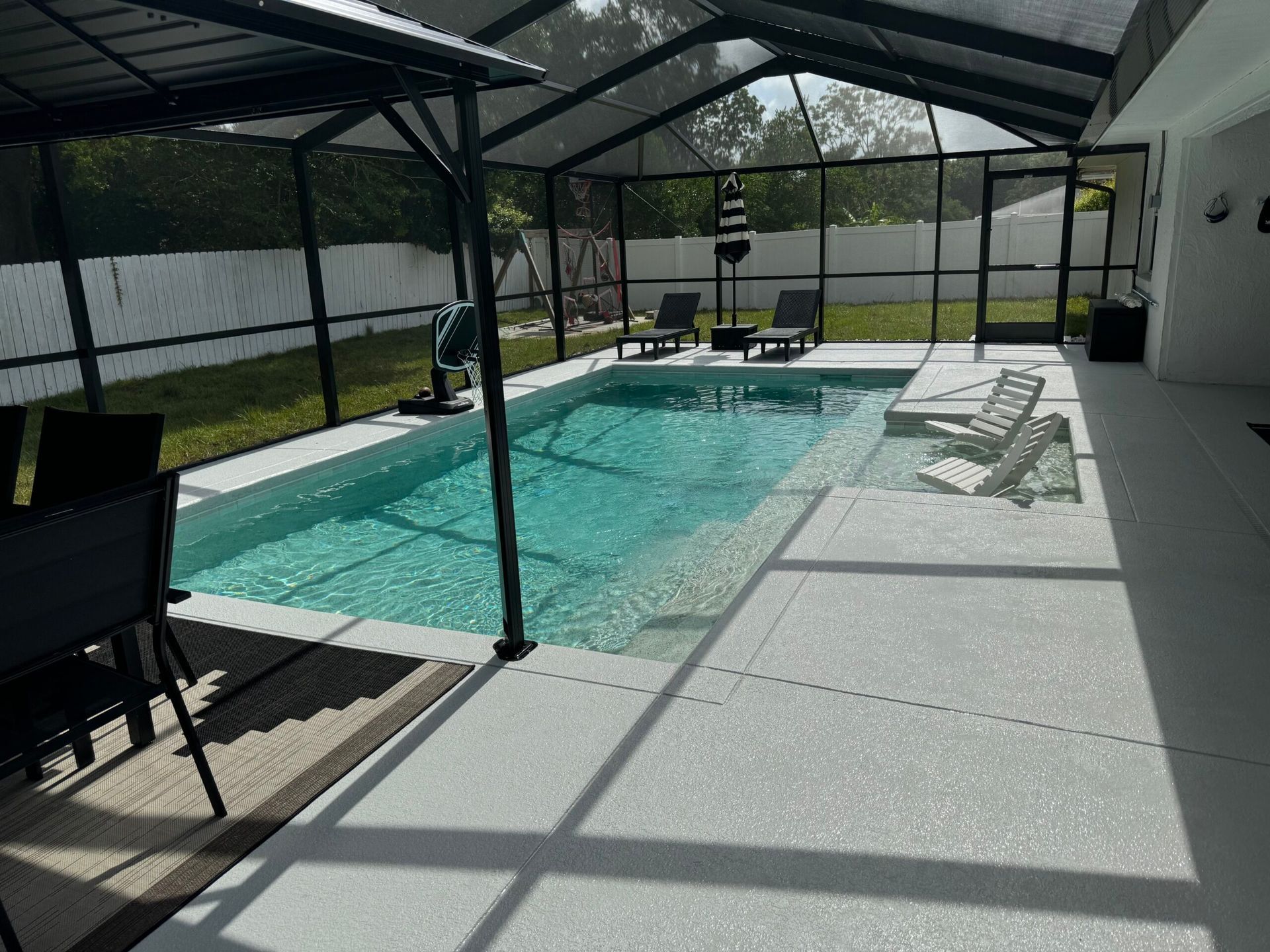 A screened-in patio with a rectangular pool, lounge chairs, and outdoor furniture. Sunlight streams through the screen.
