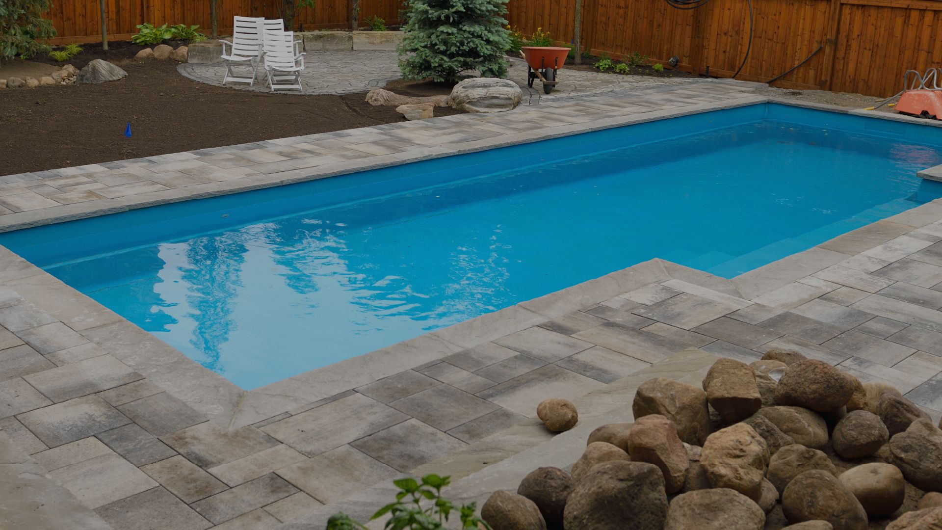 Rectangular backyard pool with blue water, surrounded by stone pavers and landscaping.