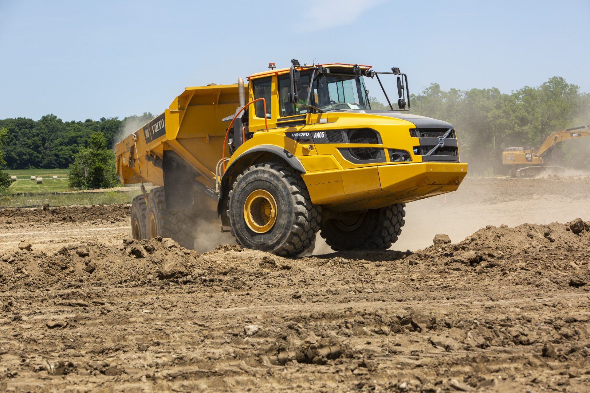 A yellow dump truck is driving through a dirt field.