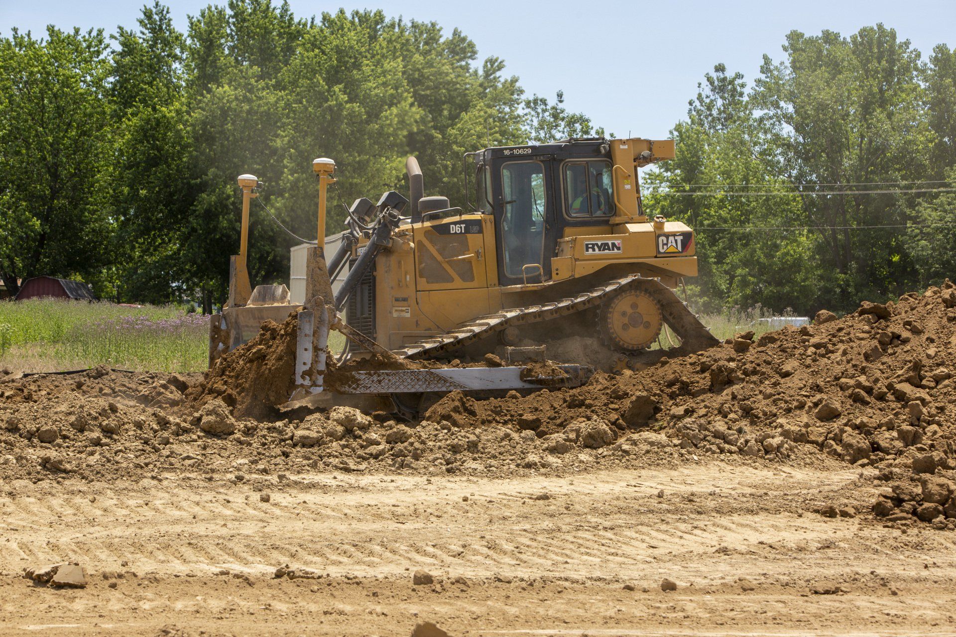 A bulldozer is moving dirt in a field with trees in the background