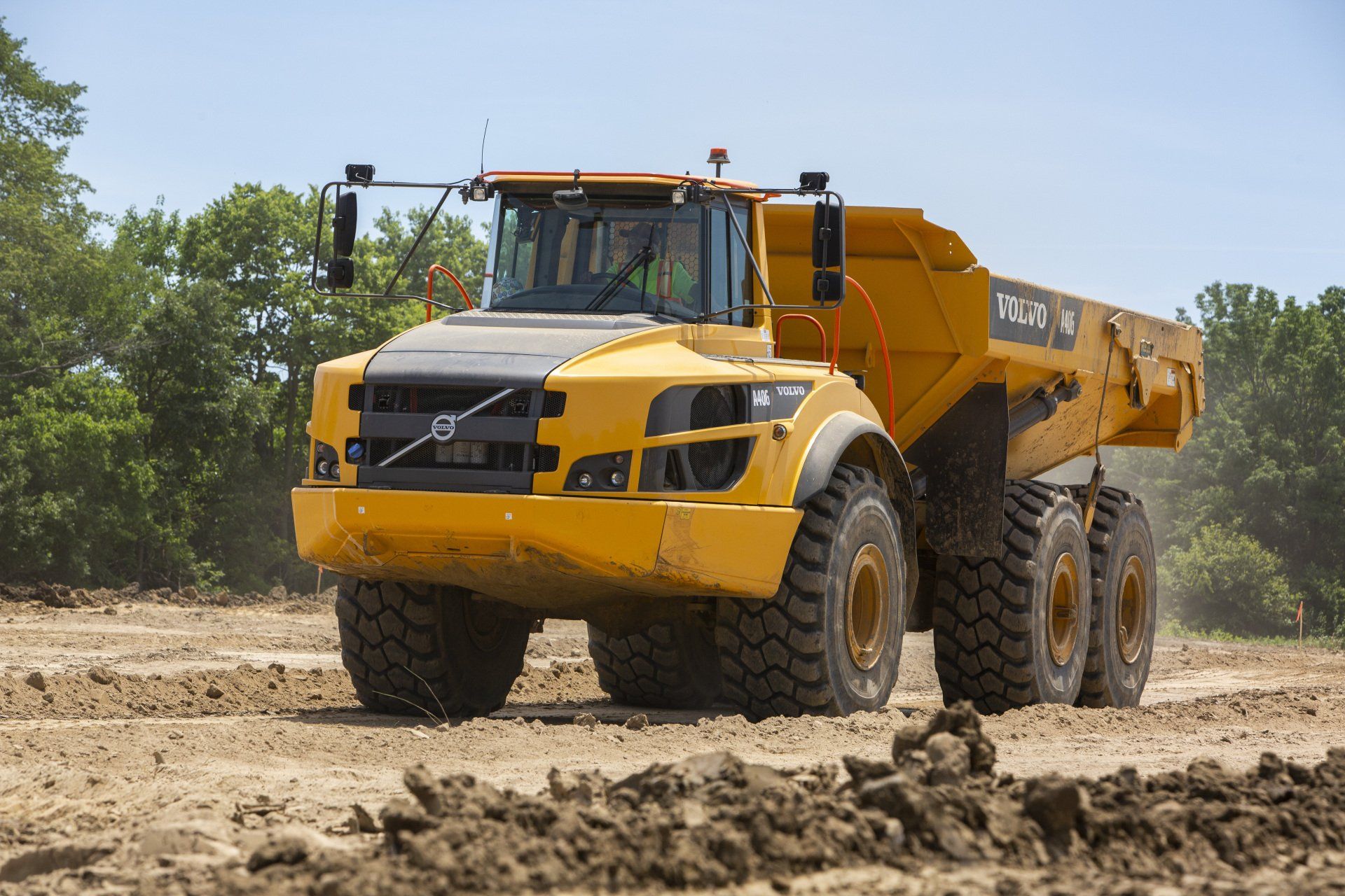 A yellow dump truck is driving through a dirt field.