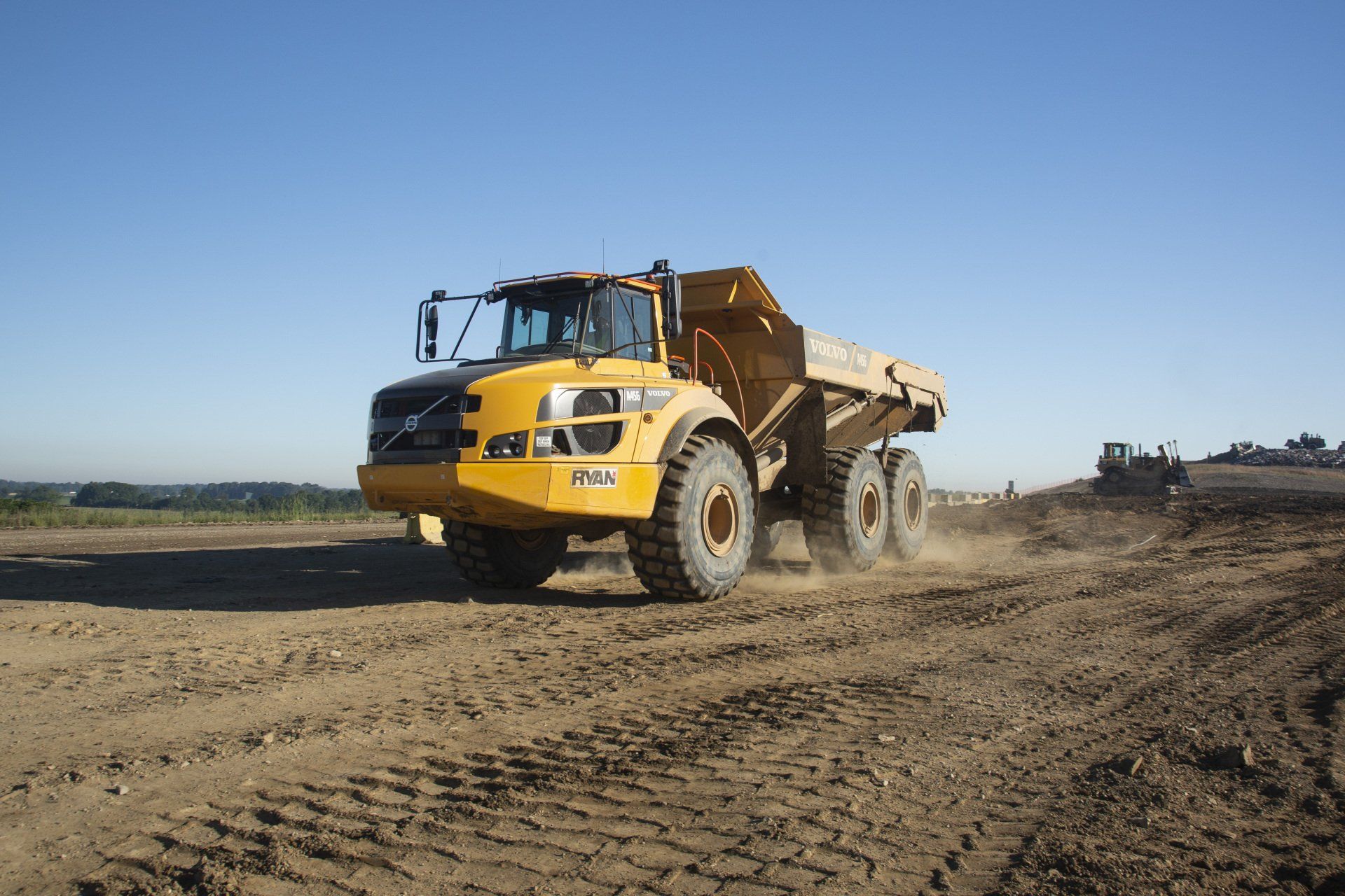 A yellow dump truck is driving through a dirt field.