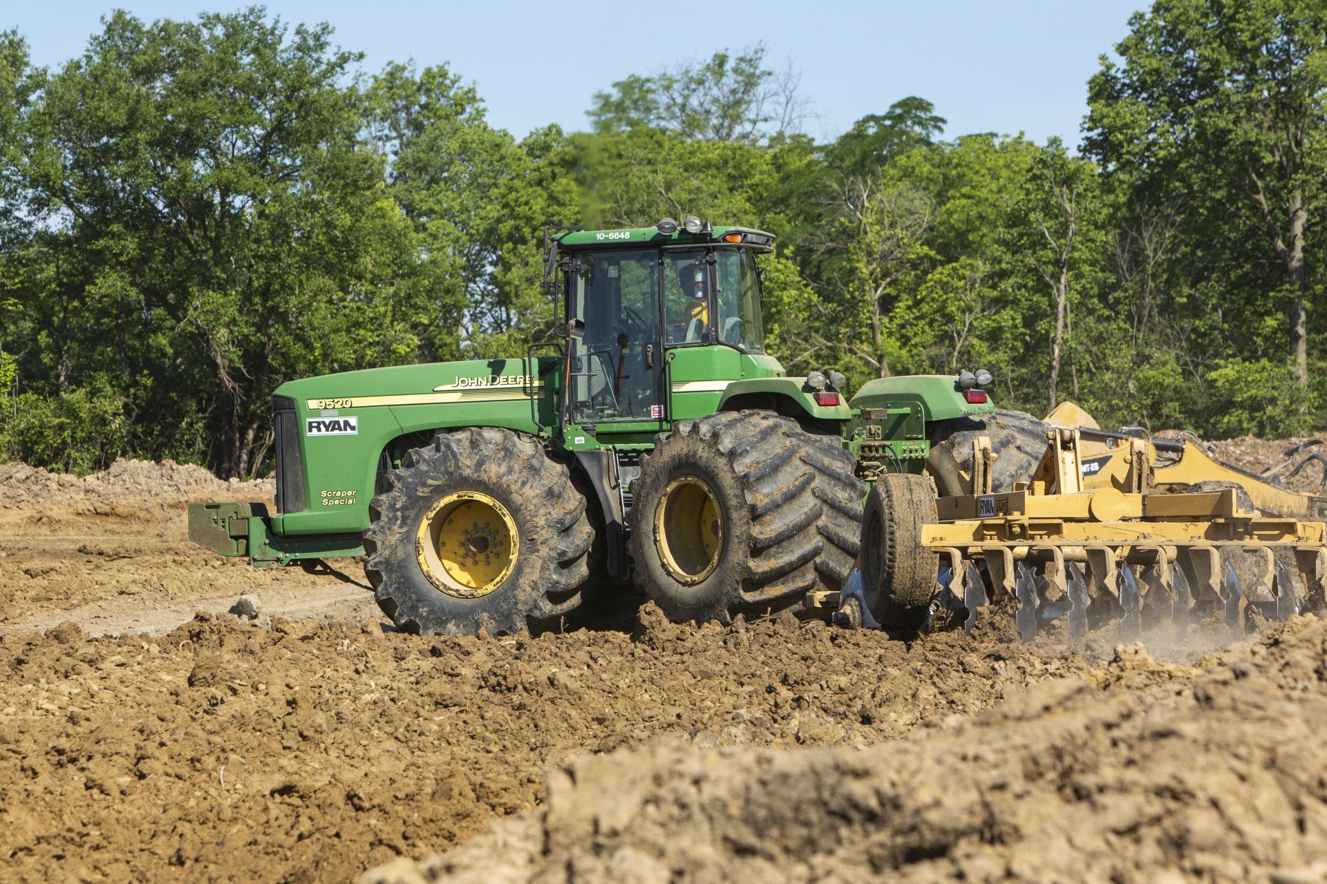 A john deere tractor is plowing a muddy field