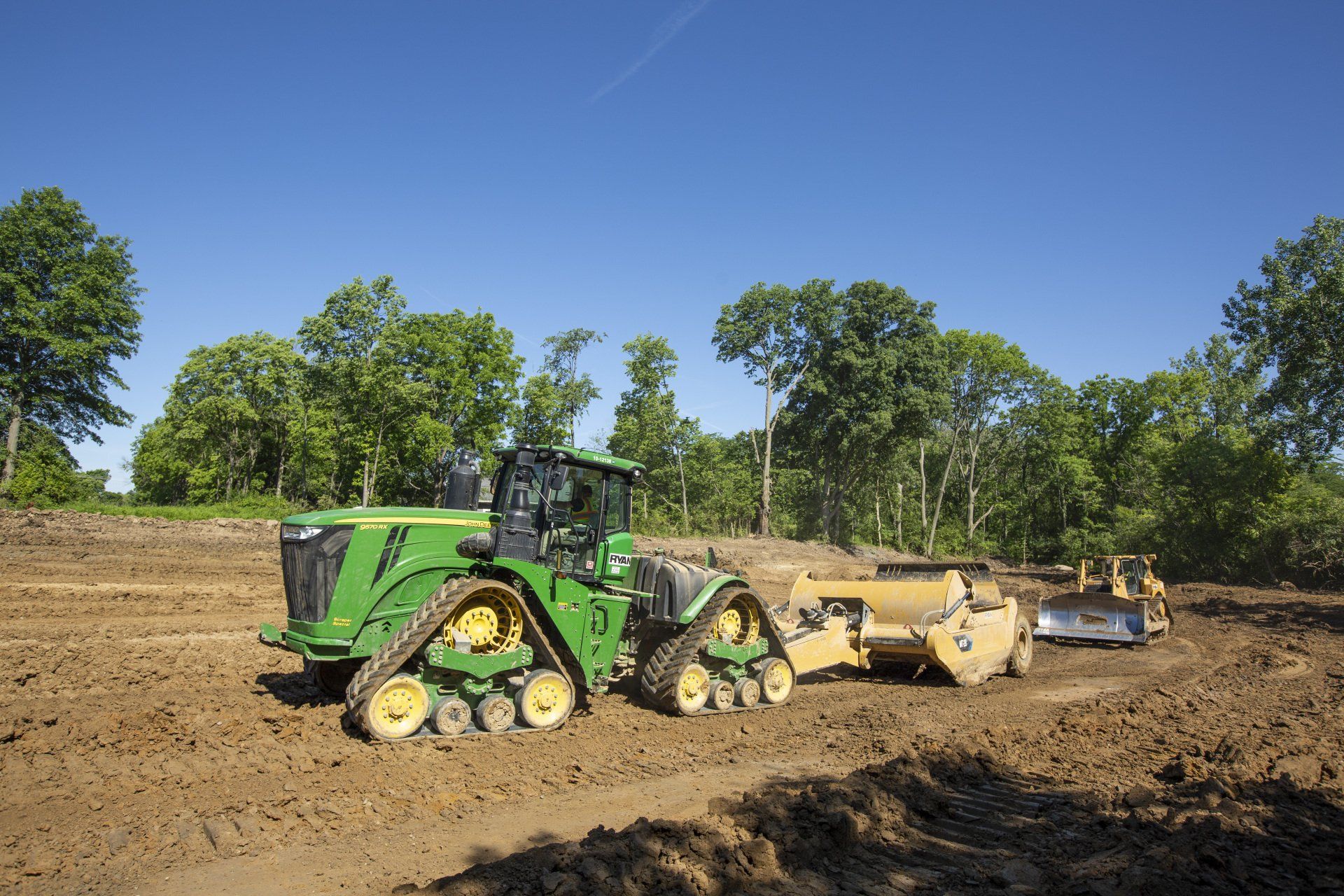 A green tractor is pulling a yellow bulldozer through a dirt field.