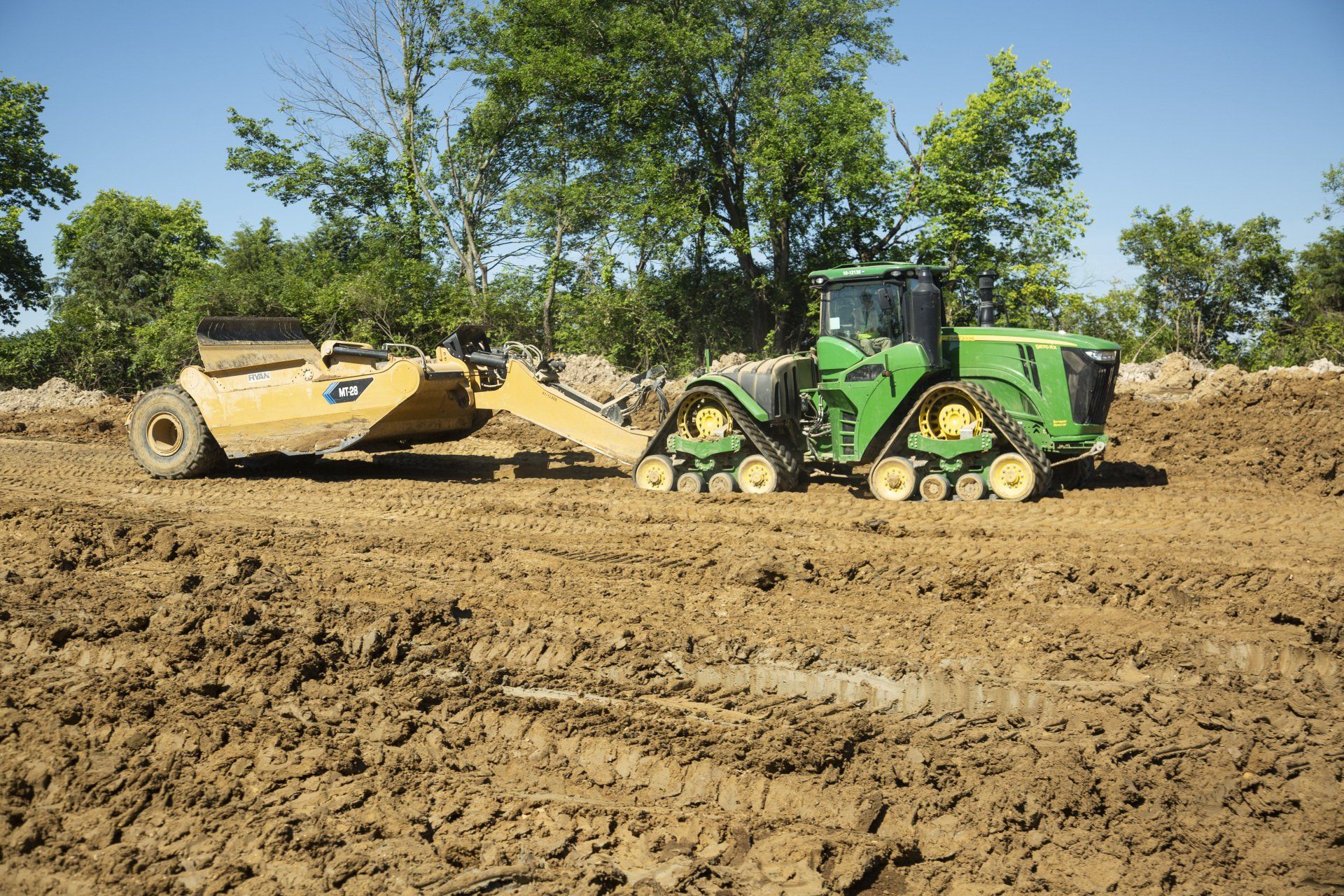 A green and yellow tractor is plowing a muddy field.