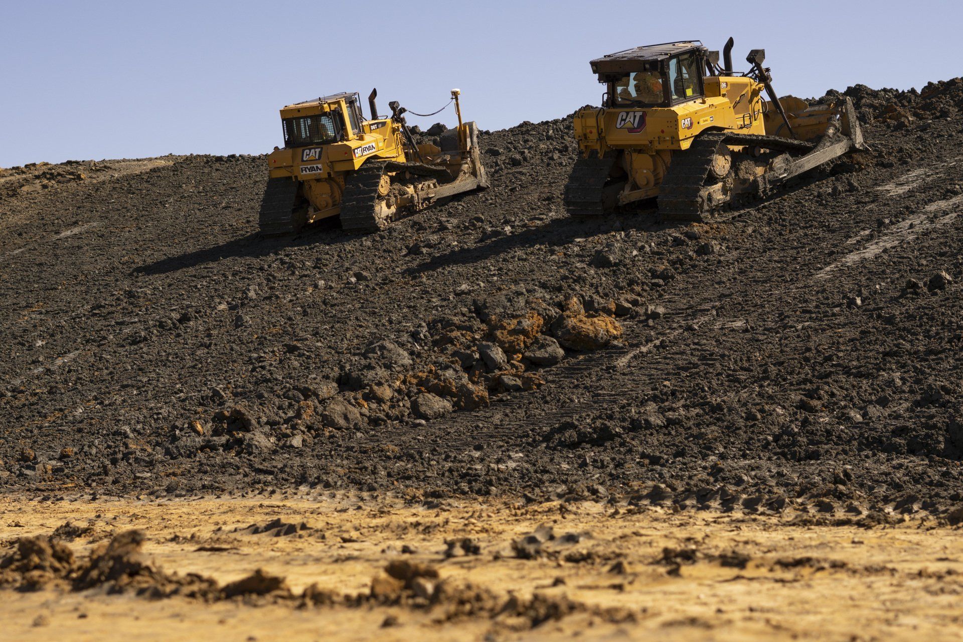 Two bulldozers are driving down a dirt hill.