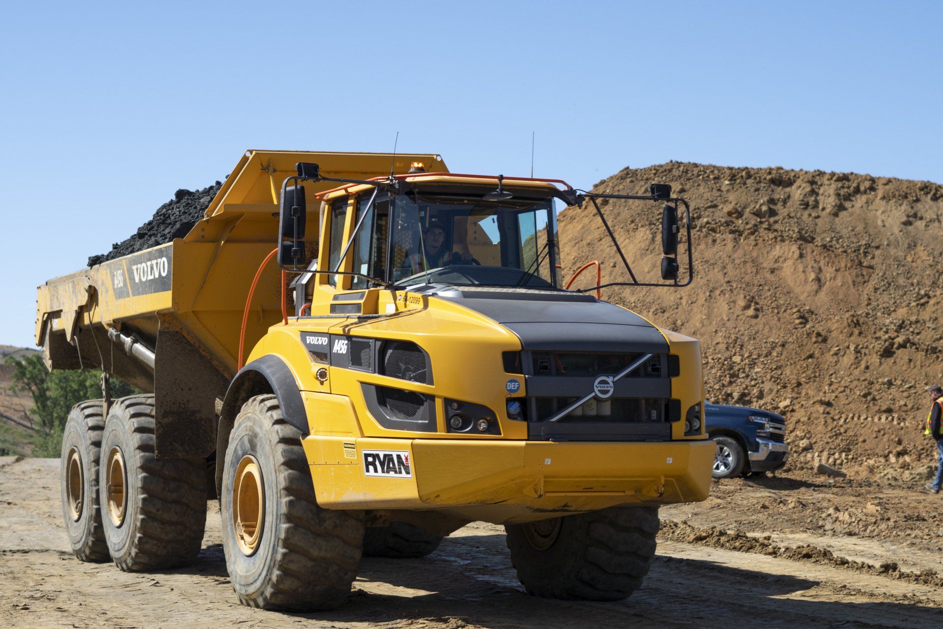 A large yellow dump truck is parked on a dirt road.