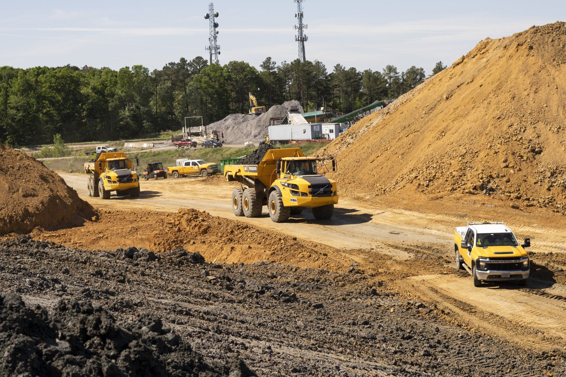A group of construction trucks are driving down a dirt road