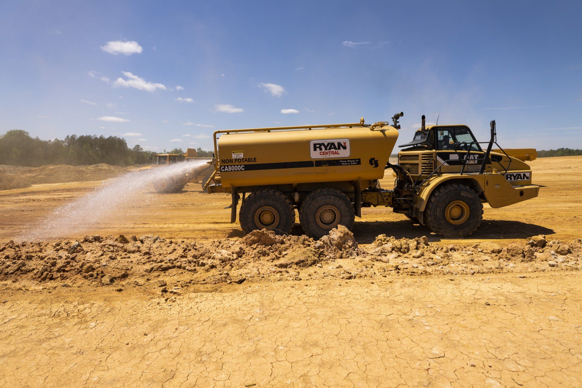 A large yellow truck is spraying water on a dirt field.