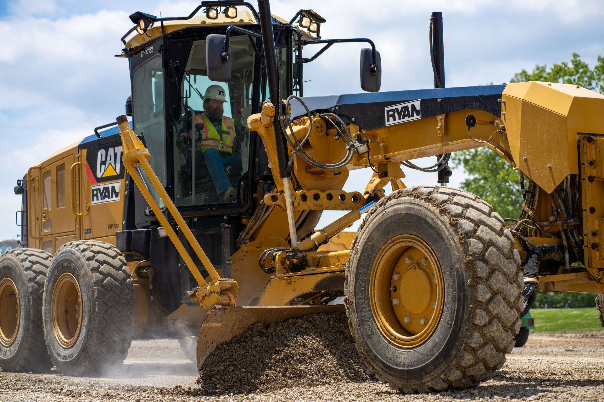 A man is driving a large yellow tractor on a dirt road.