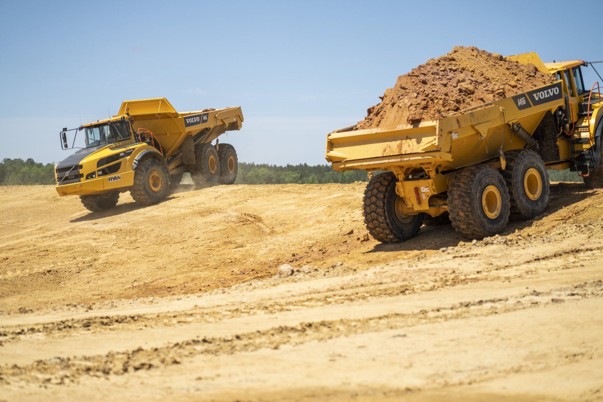 Two dump trucks are driving down a dirt road.