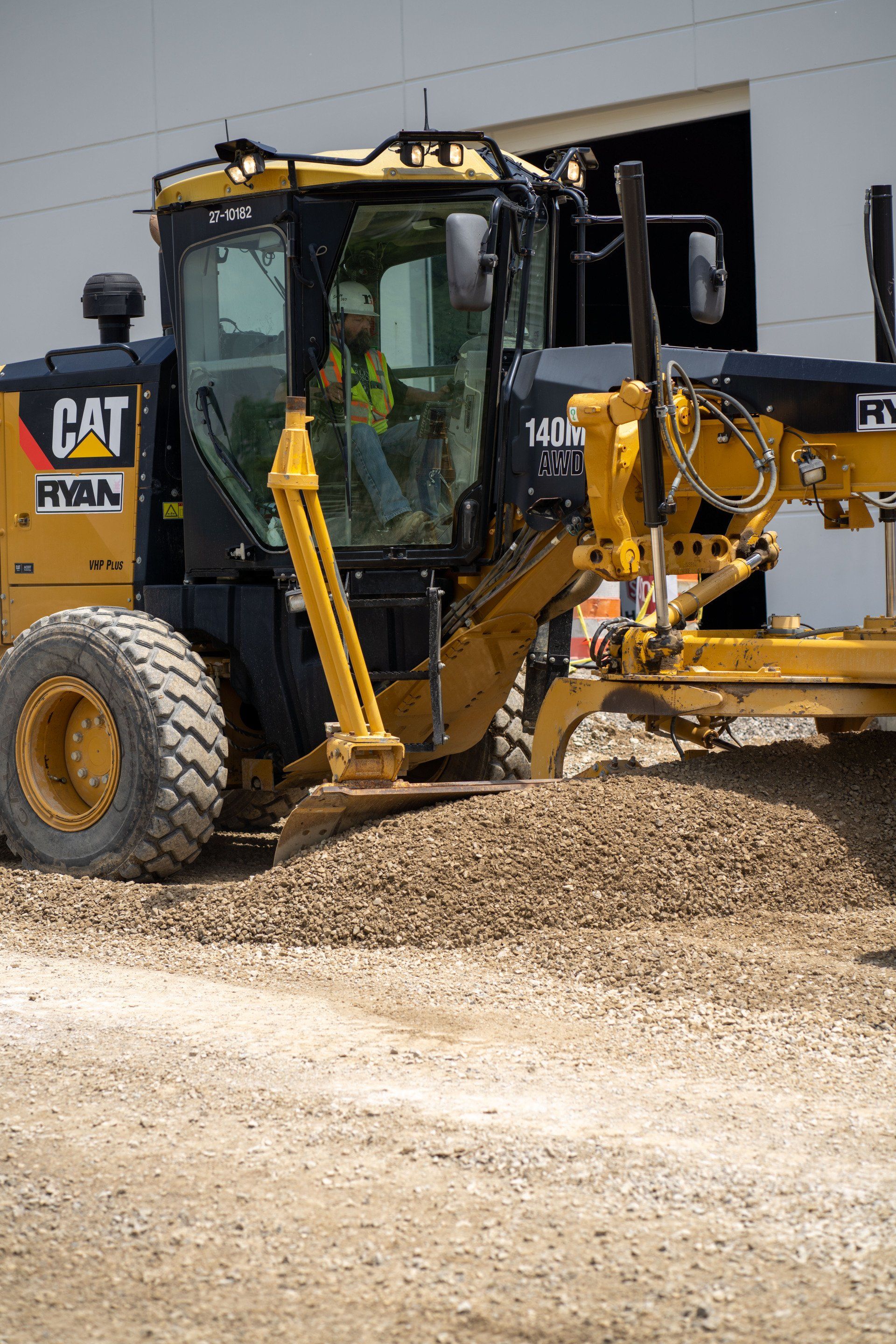 A yellow and black cat grader is sitting on top of a pile of gravel.