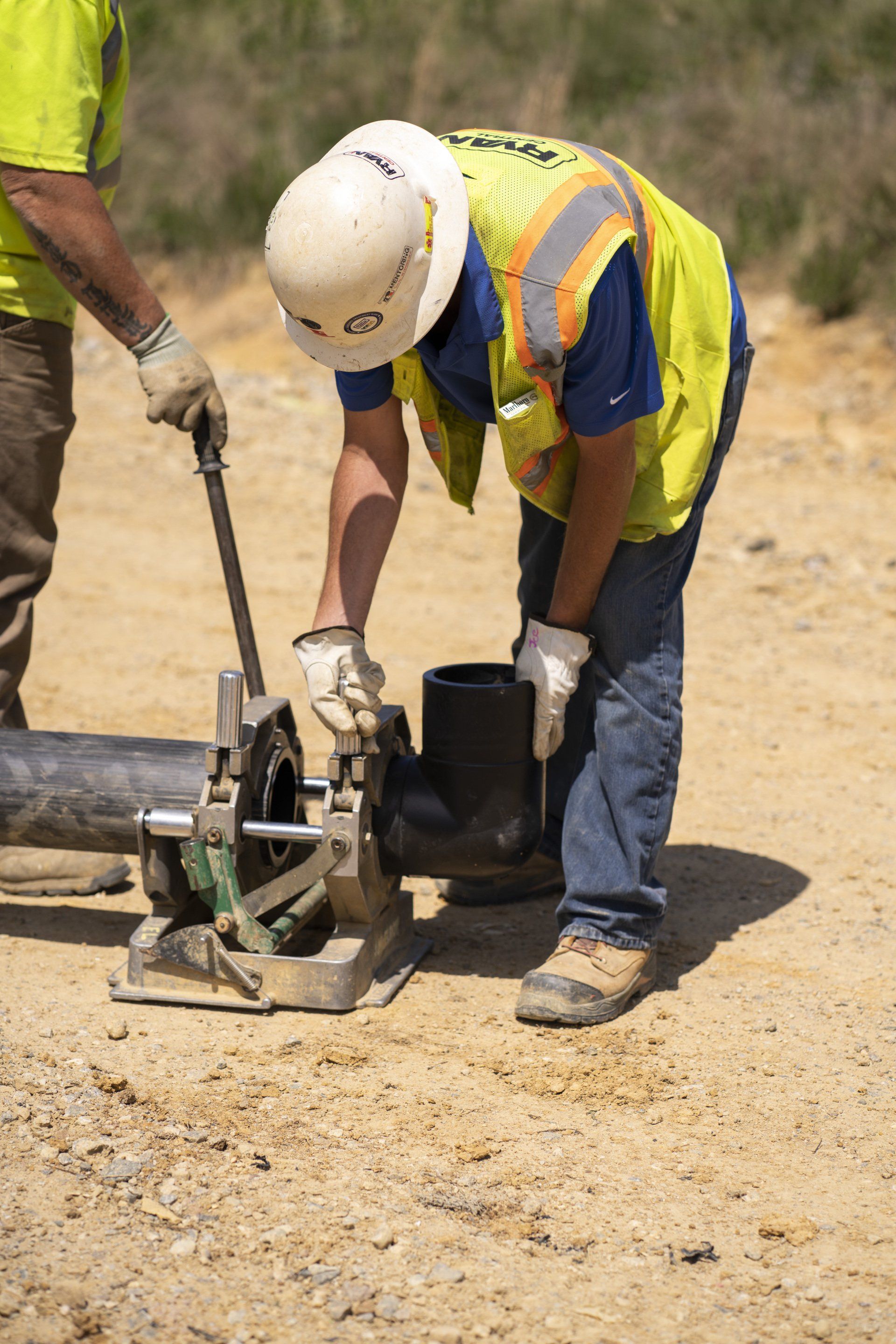 A man wearing a hard hat and safety vest is working on a pipe.