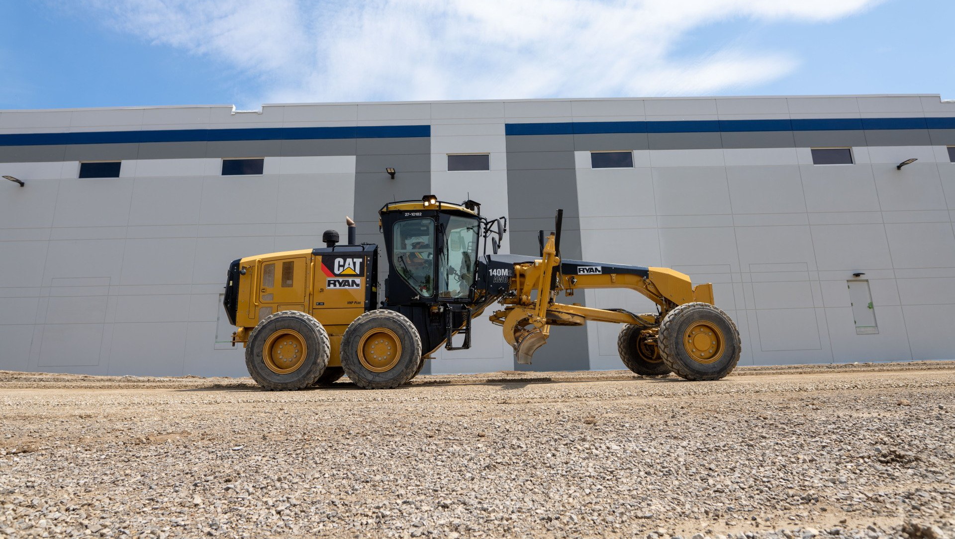 A bulldozer is driving down a dirt road in front of a building.