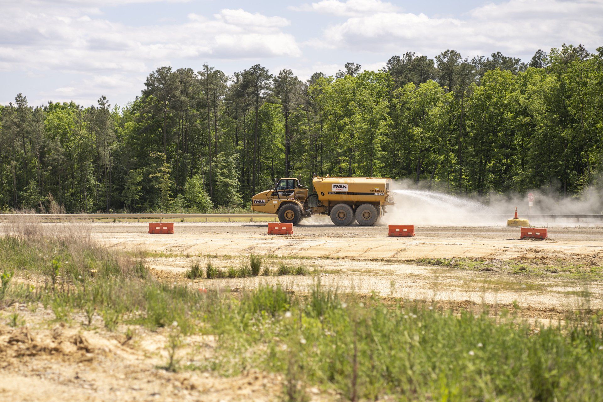 A large yellow truck is spraying water on a dirt road.