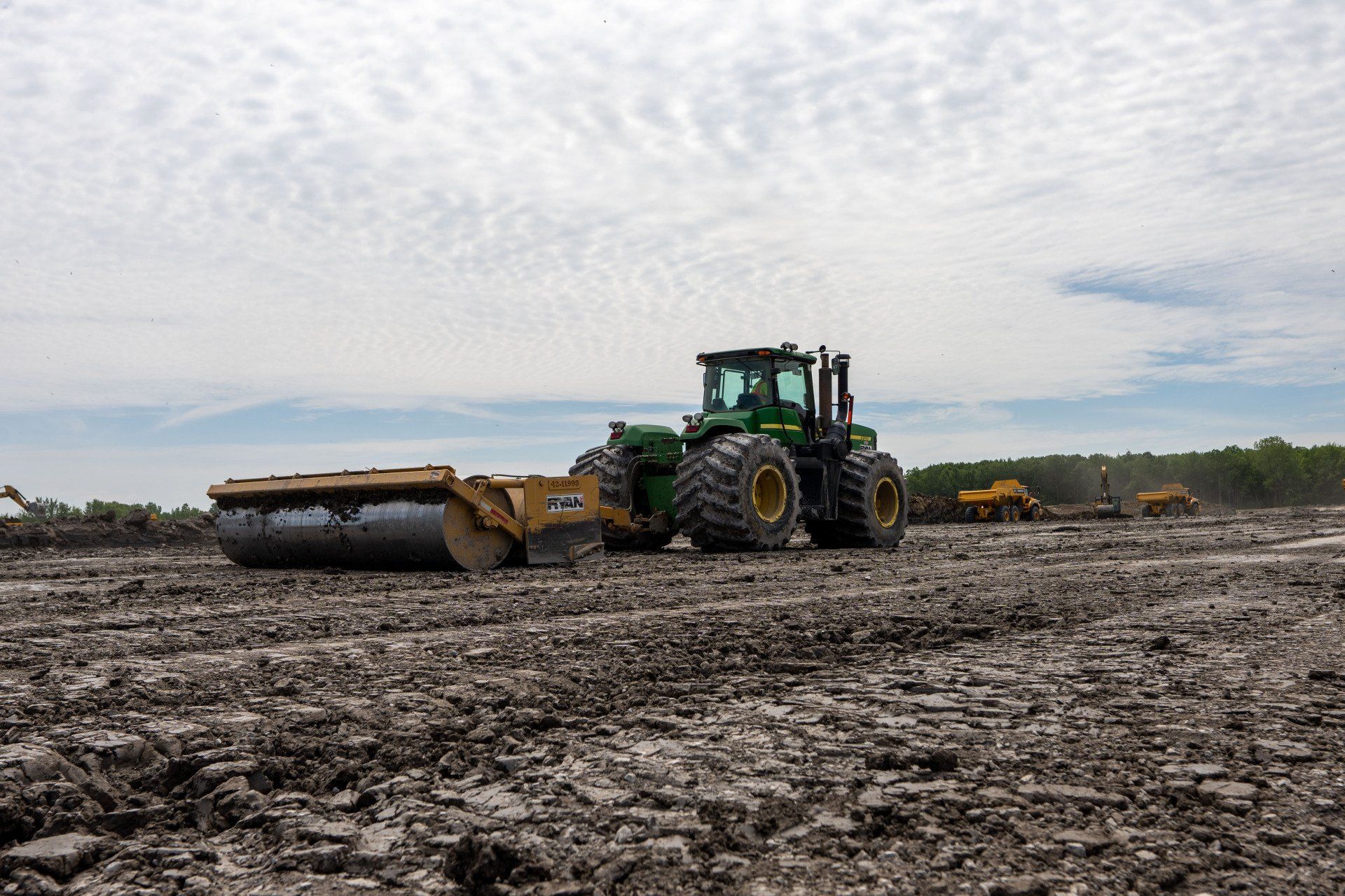 A green tractor is driving through a muddy field.