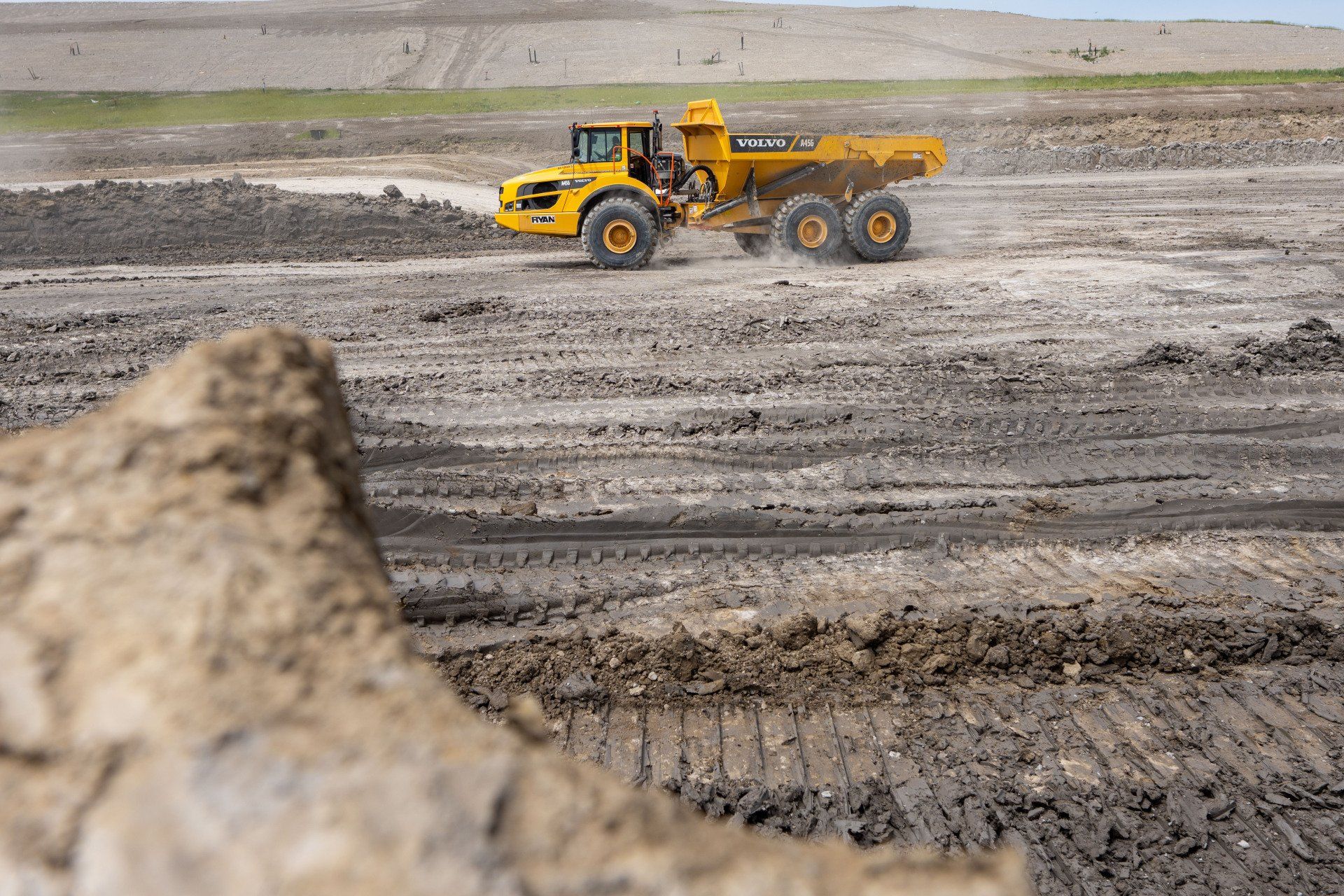 A yellow dump truck is driving through a dirt field.