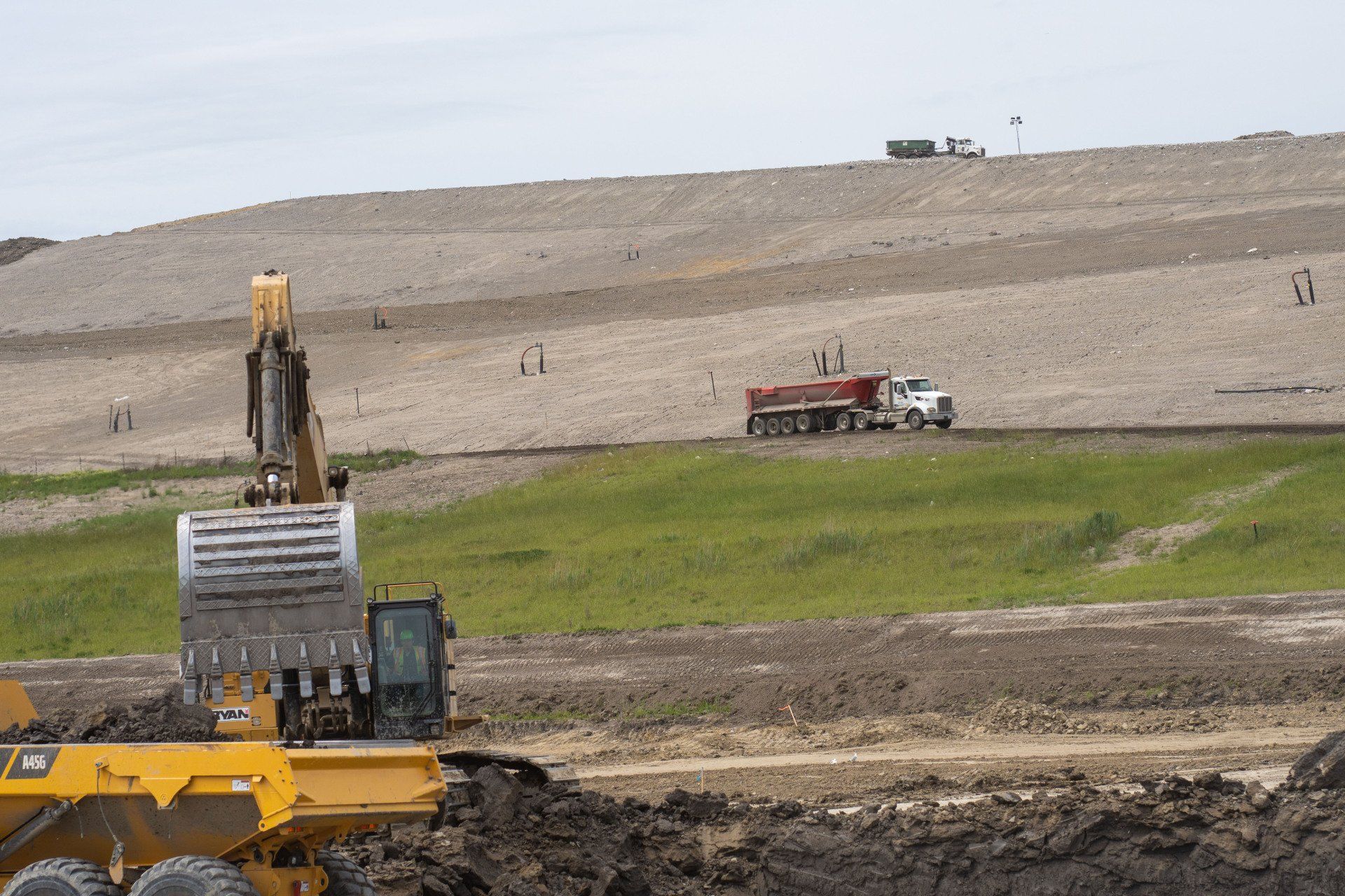 A dump truck is driving down a dirt road next to a bulldozer.