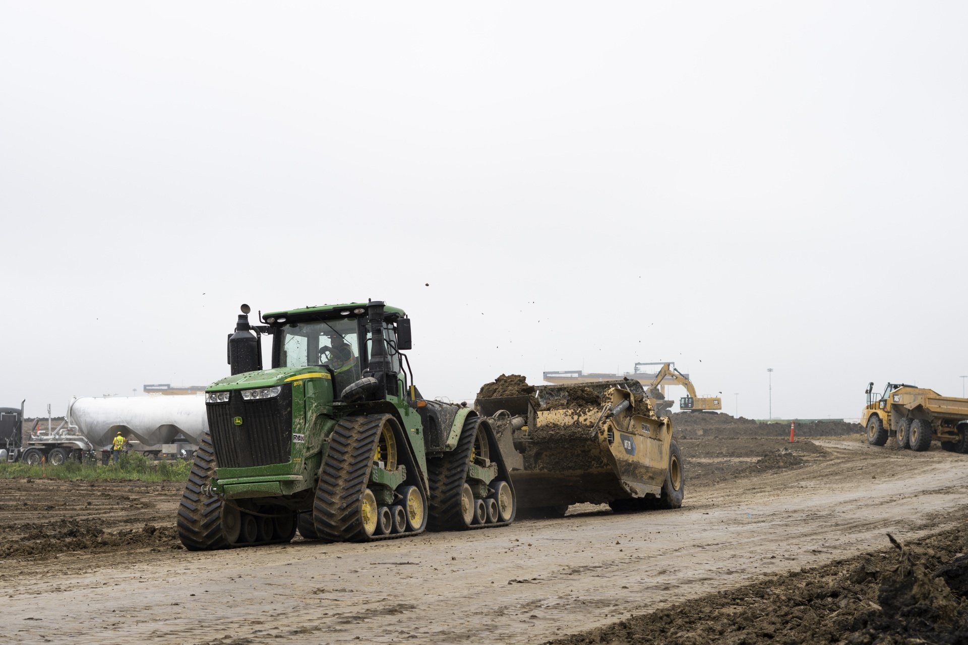 A green tractor is pulling a yellow dump truck on a dirt road.
