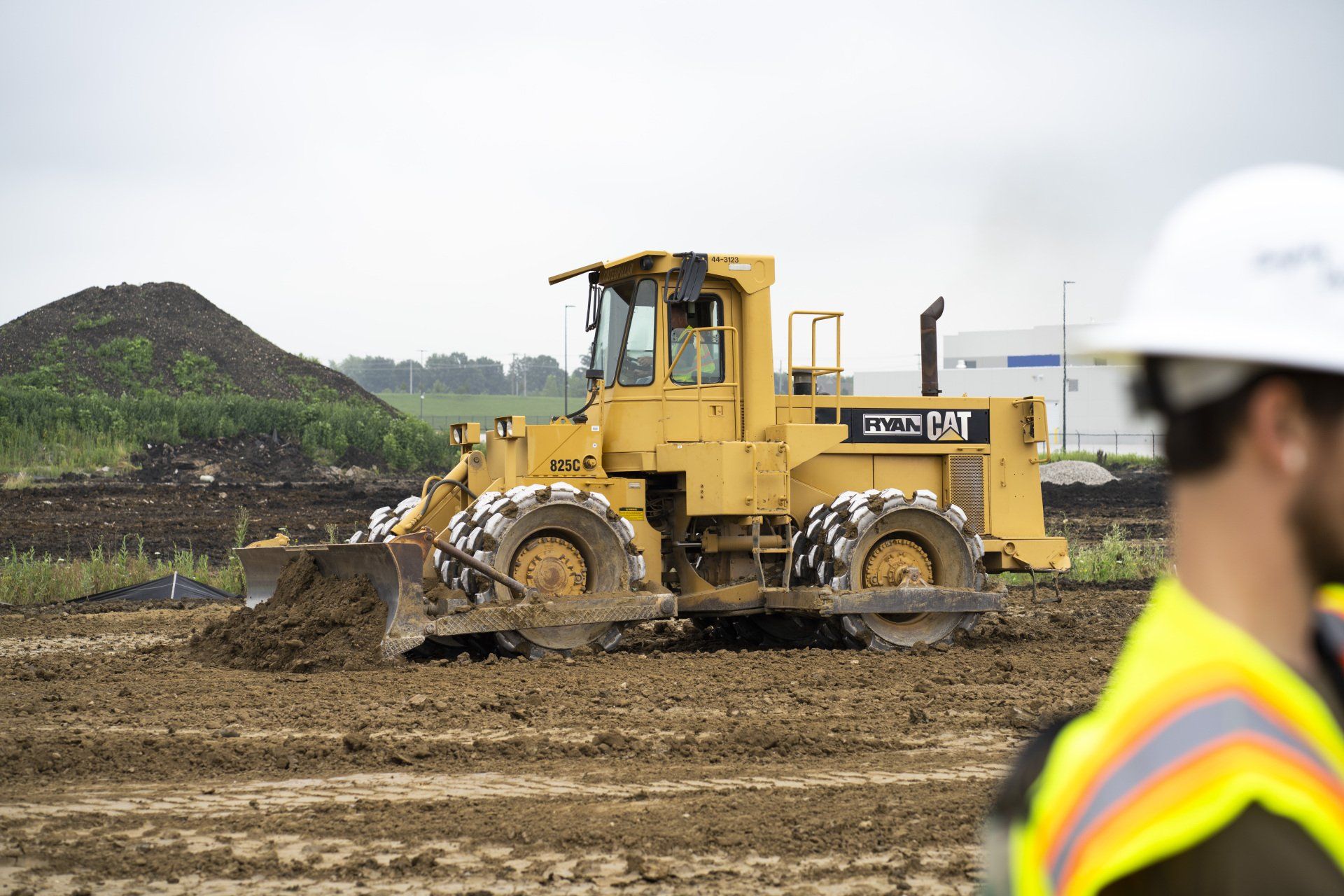 A man in a hard hat is looking at a bulldozer in a field.