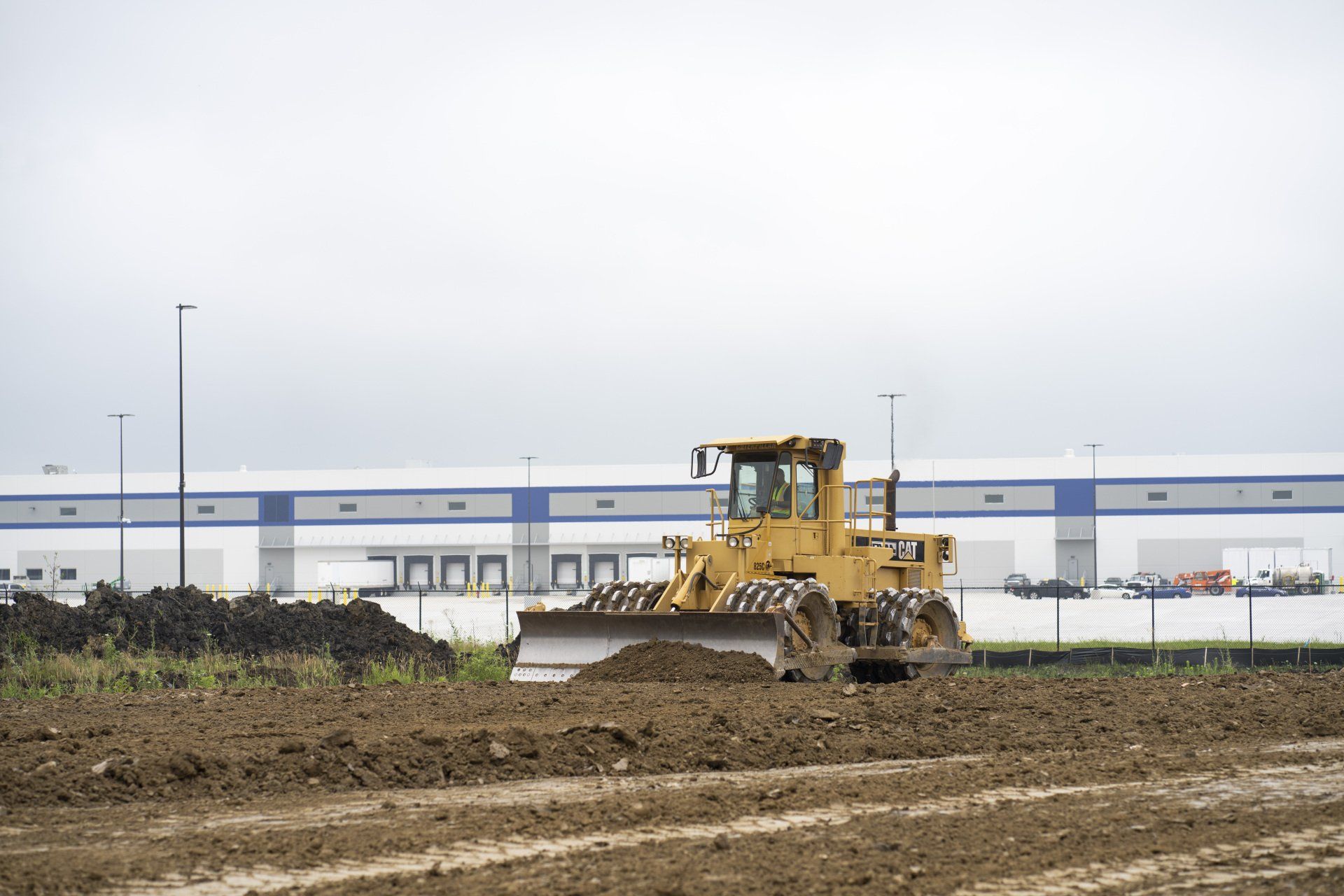 A bulldozer is moving dirt in a field in front of a large building.