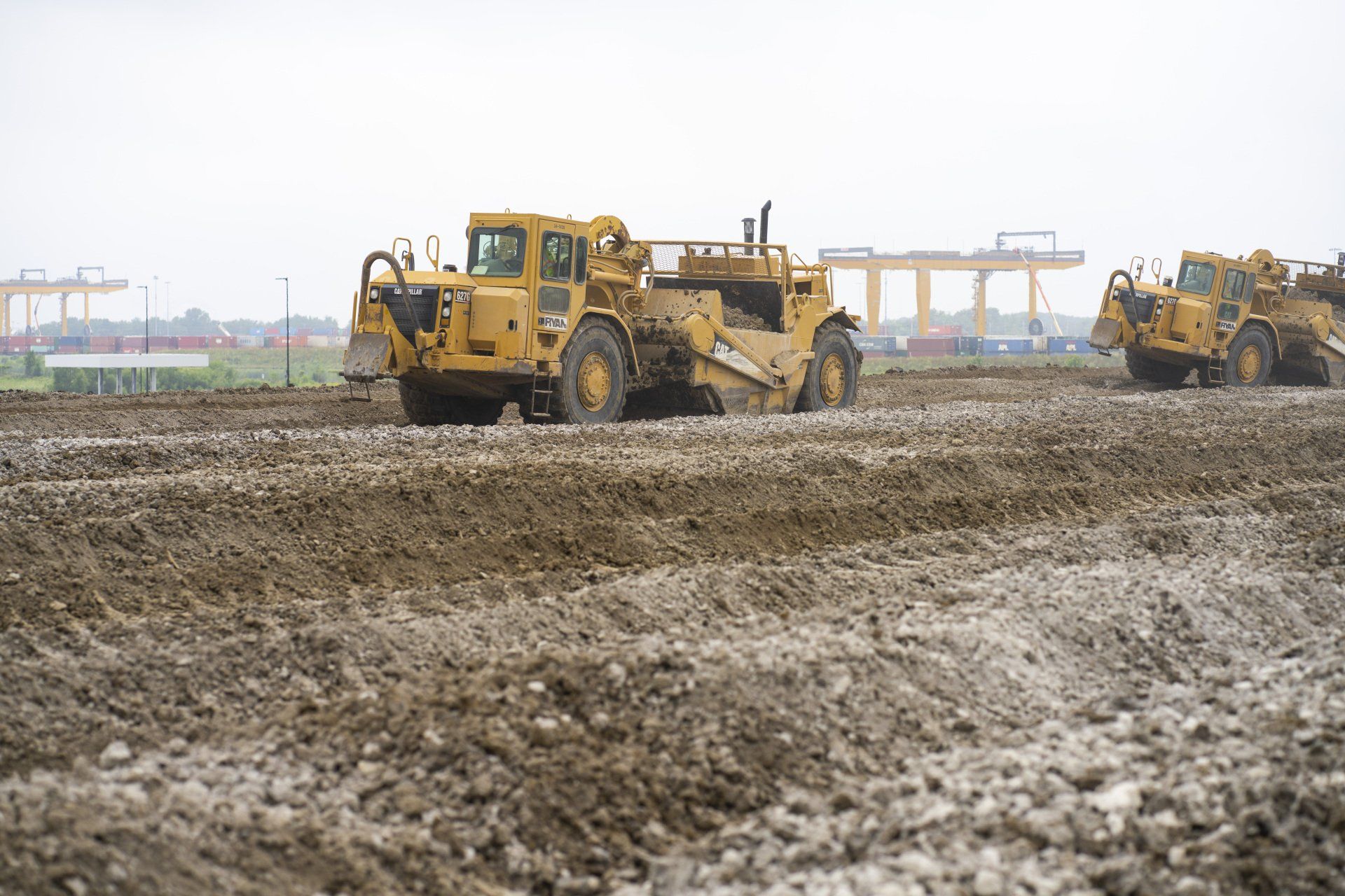 A couple of bulldozers are driving through a muddy field.