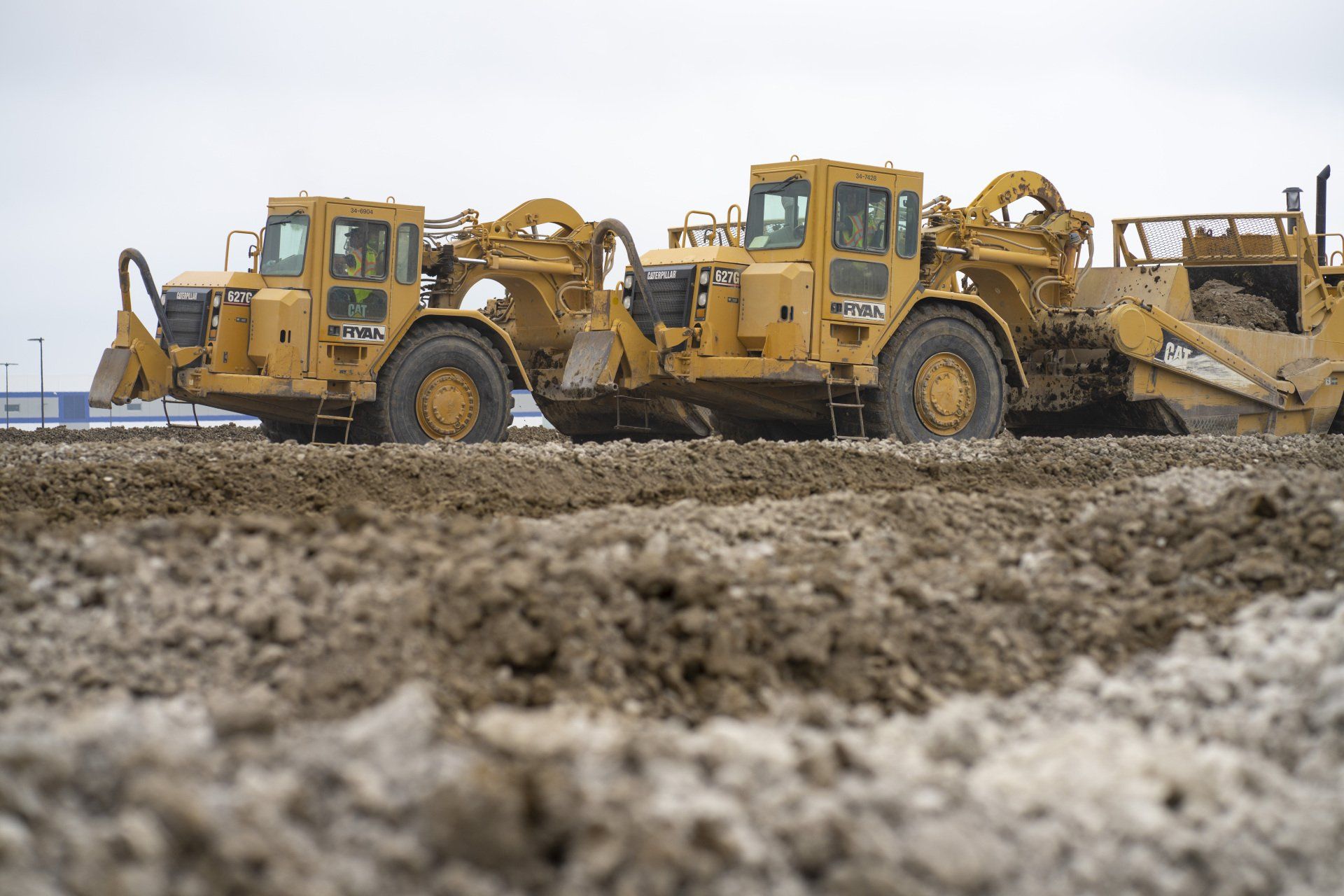 Two bulldozers are driving through a muddy field.