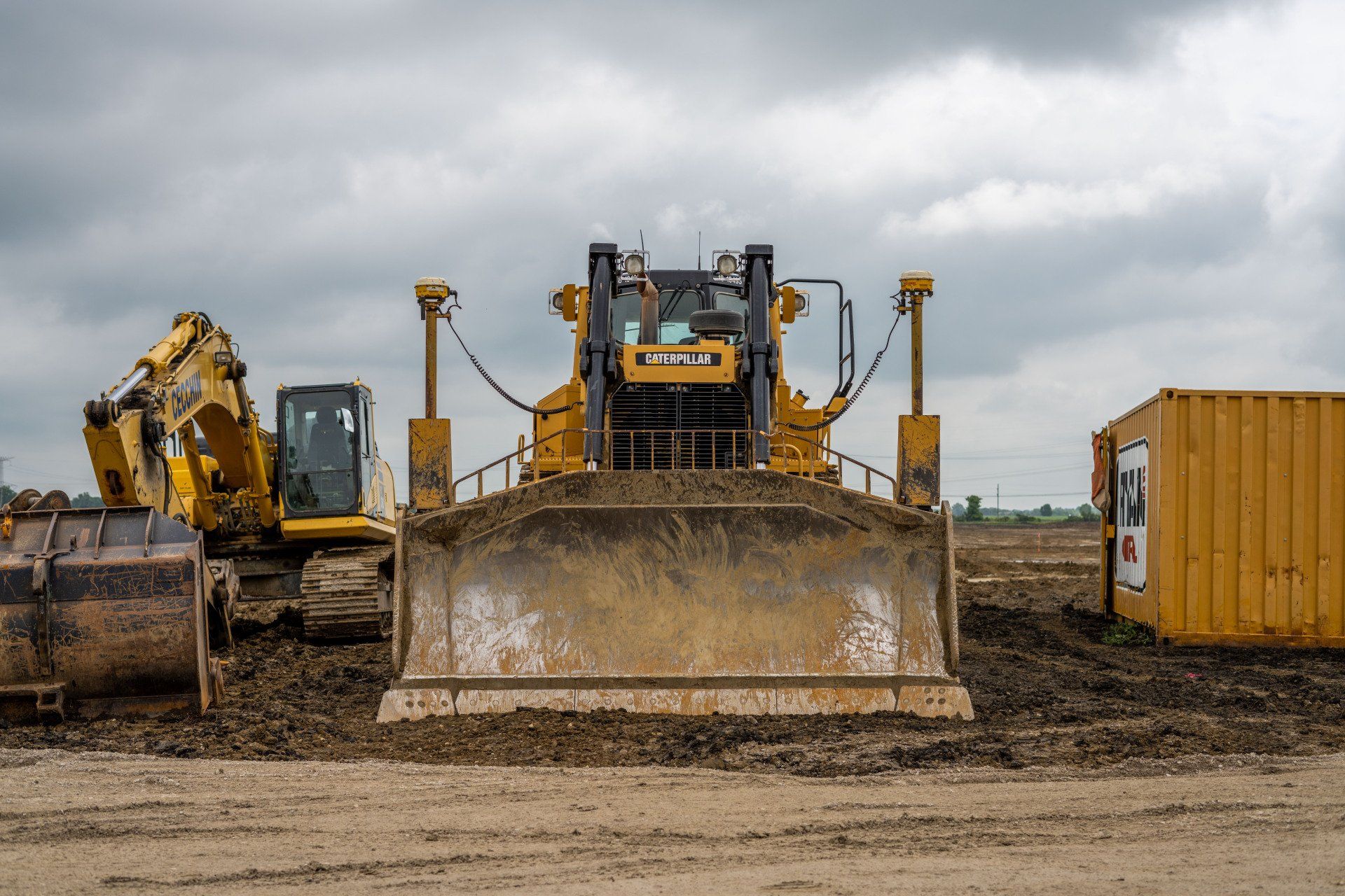 A bulldozer is sitting on top of a dirt field next to a yellow container.