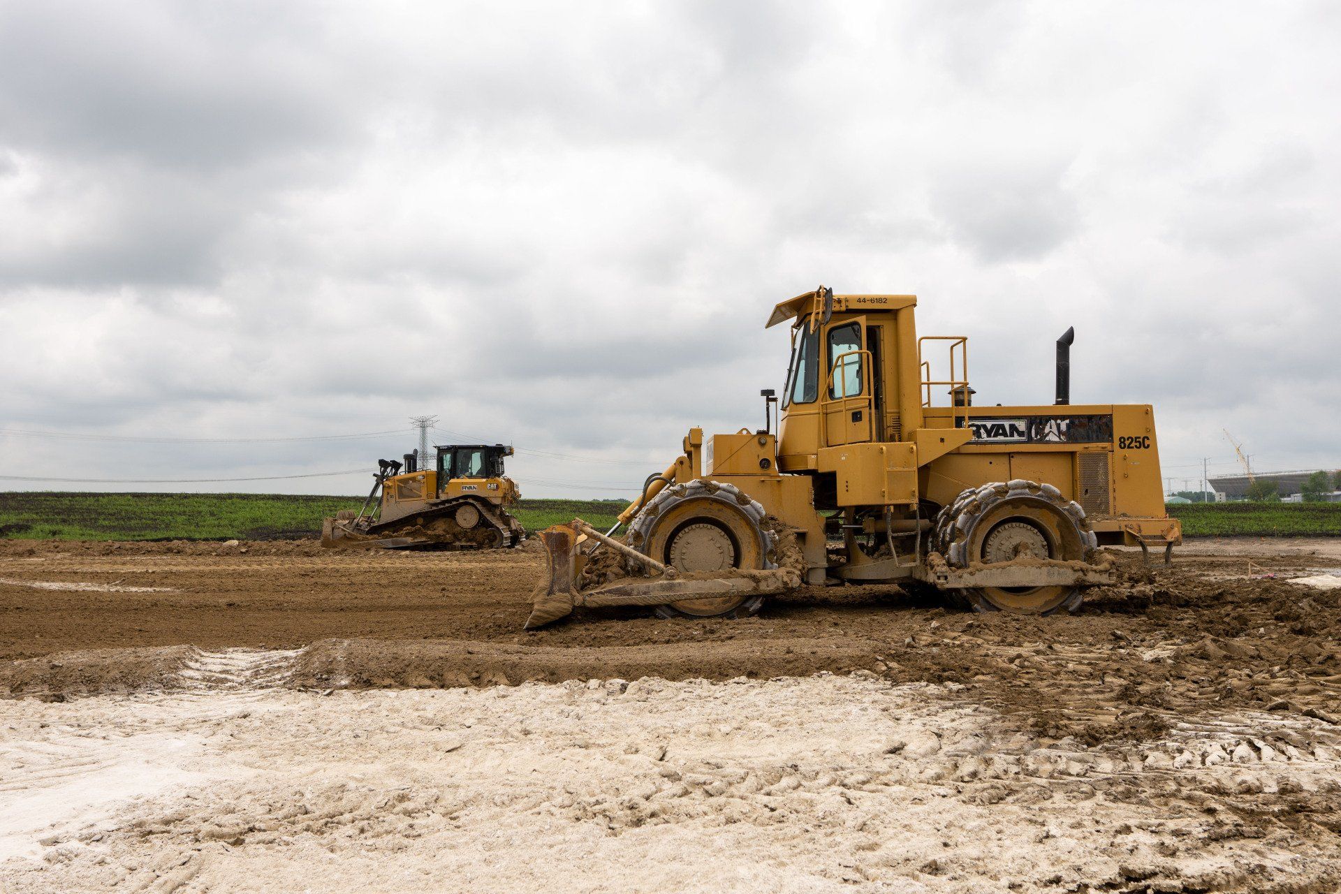Two bulldozers are working in a muddy field.