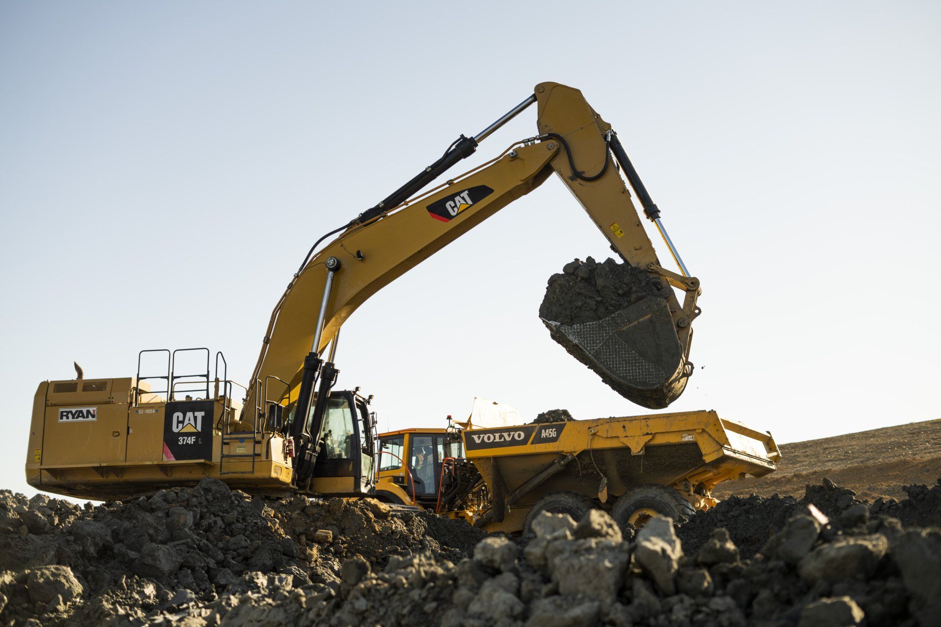 A large yellow excavator is loading rocks into a dump truck.
