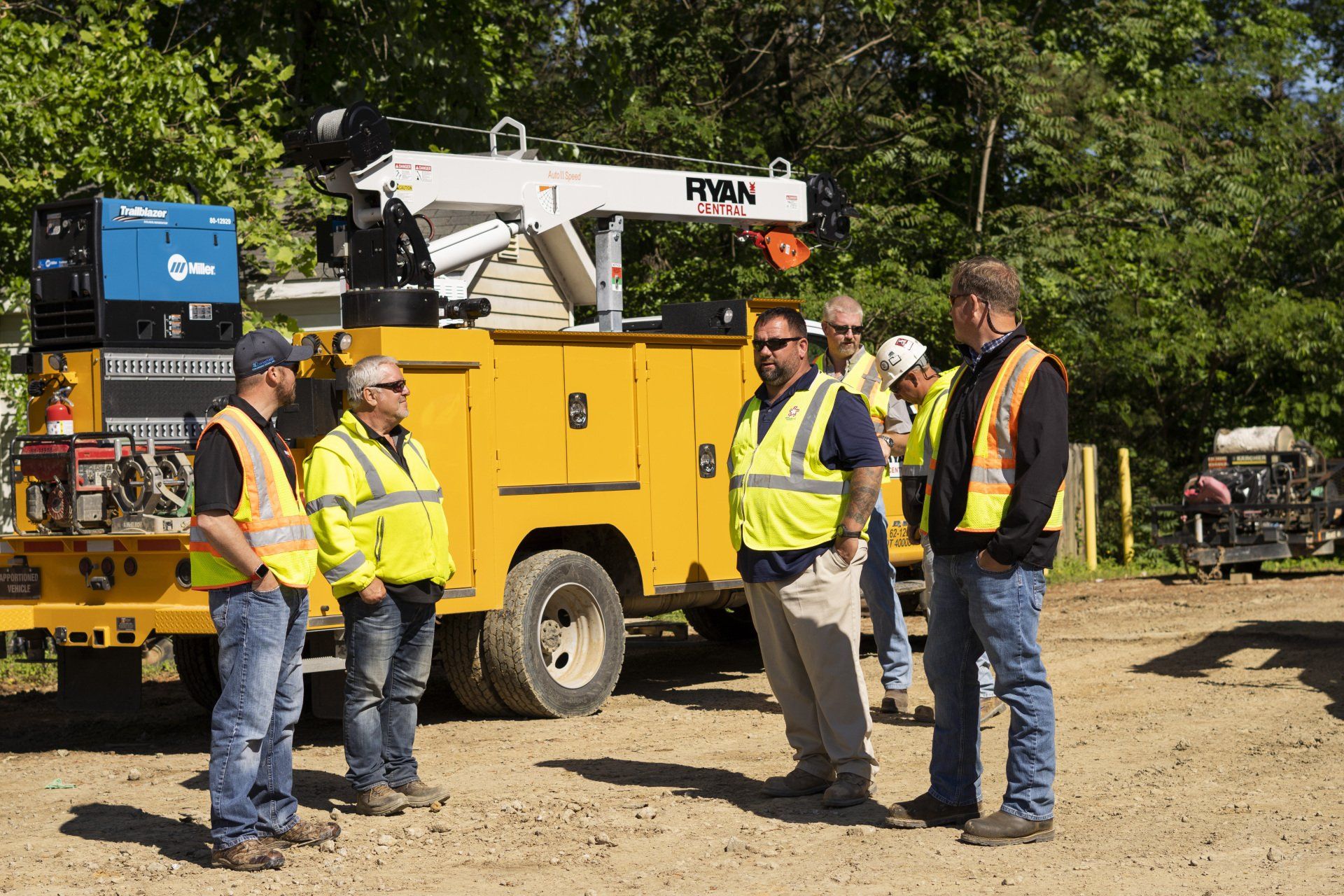 A group of construction workers are standing in front of a yellow truck.