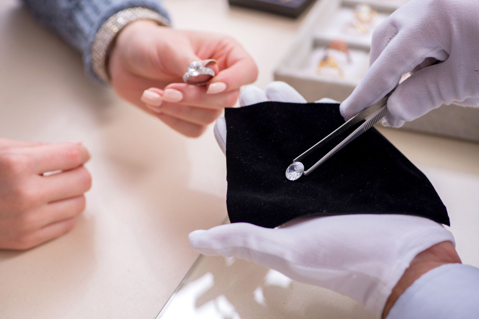 Jeweler holding diamond with tweezers while showing a ring to a customer.
