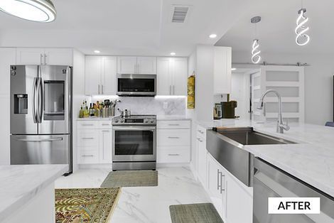 Modern white kitchen with stainless steel appliances, marble countertops, and a farmhouse sink.