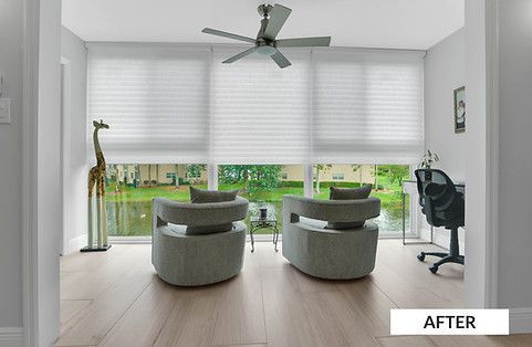 A room with two gray chairs, a desk, a giraffe statue, and a ceiling fan in front of large windows with blinds.